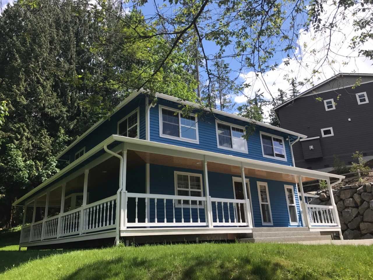 A blue house with a white porch and a black building in the background.
