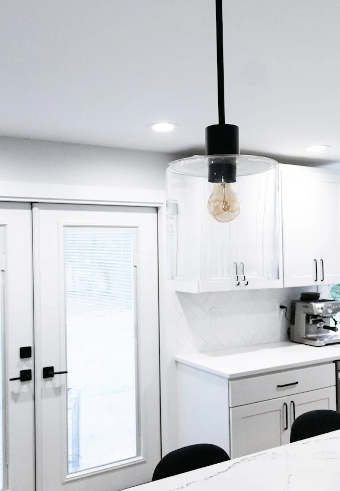 Modern kitchen with a clear glass pendant light, white cabinets, and a French door.