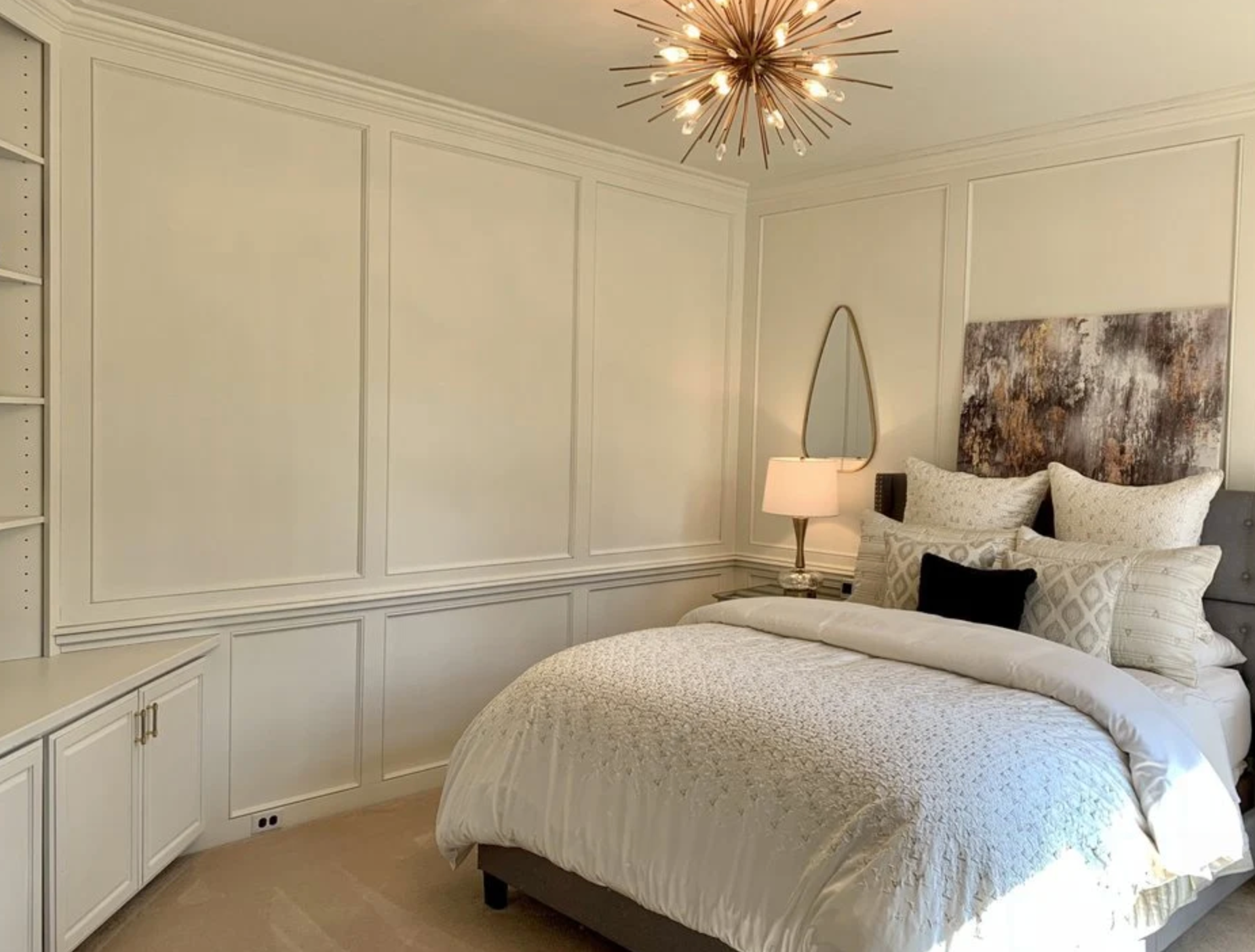 Bedroom with white paneled walls, bed, built-in shelving, and a starburst chandelier.