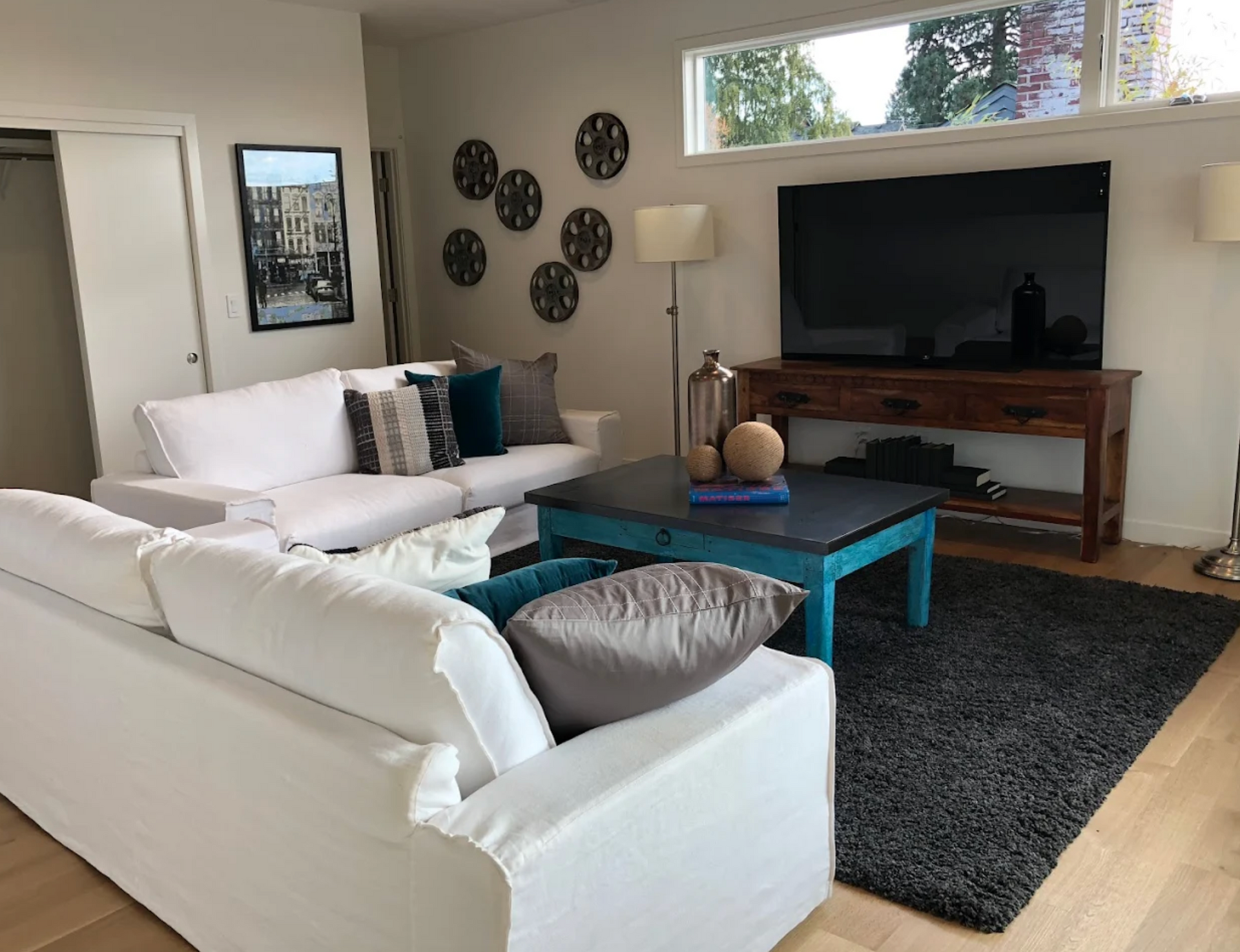 Living room with white sofas, TV on wood console, blue coffee table, and dark gray rug.