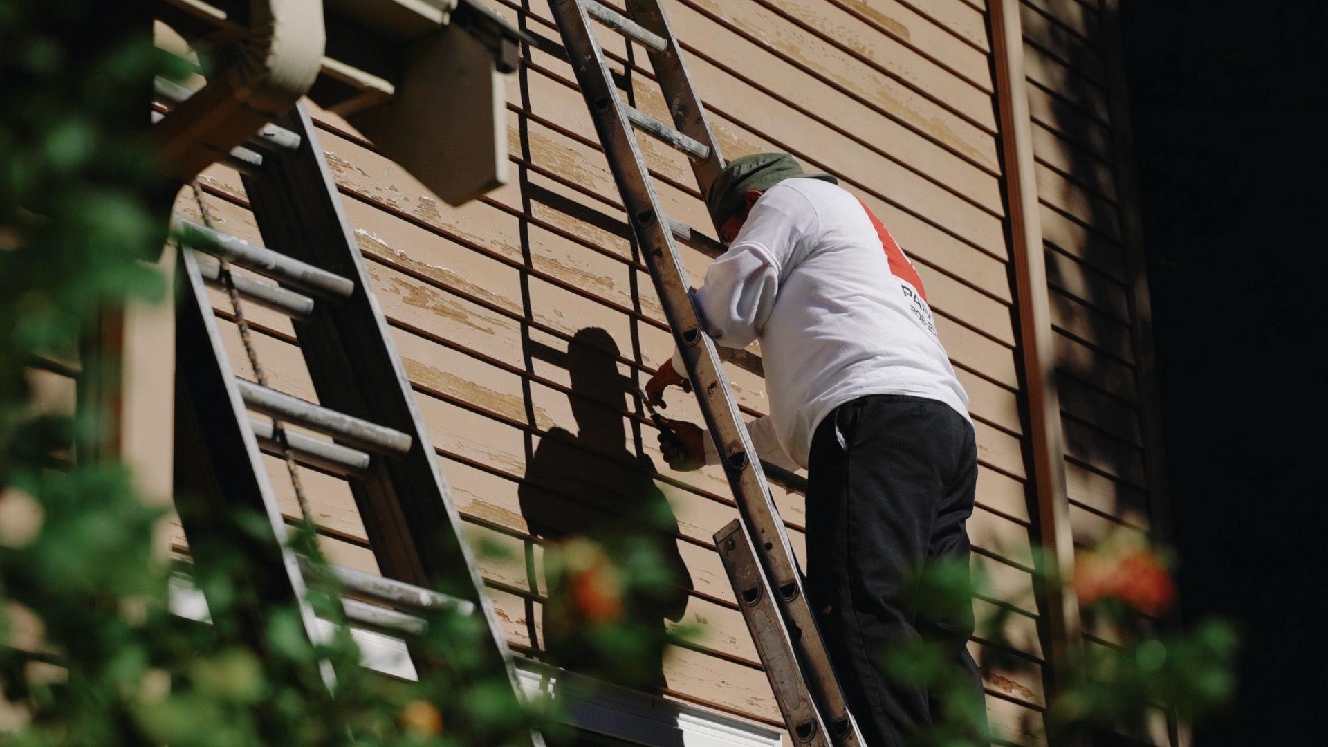 A man is climbing a ladder to paint a building.