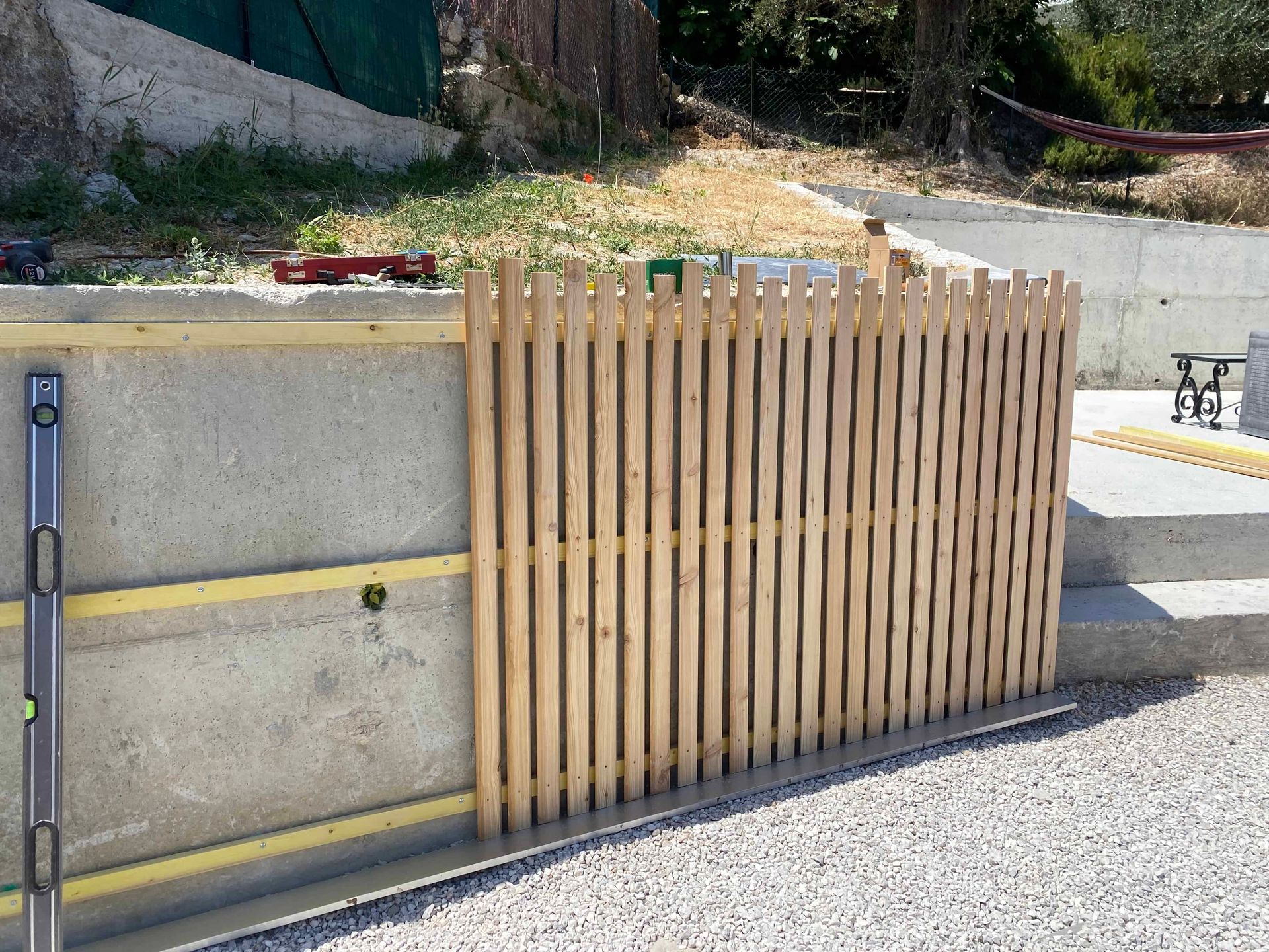 Une clôture en bois est en cours de construction à côté d'un mur en béton.