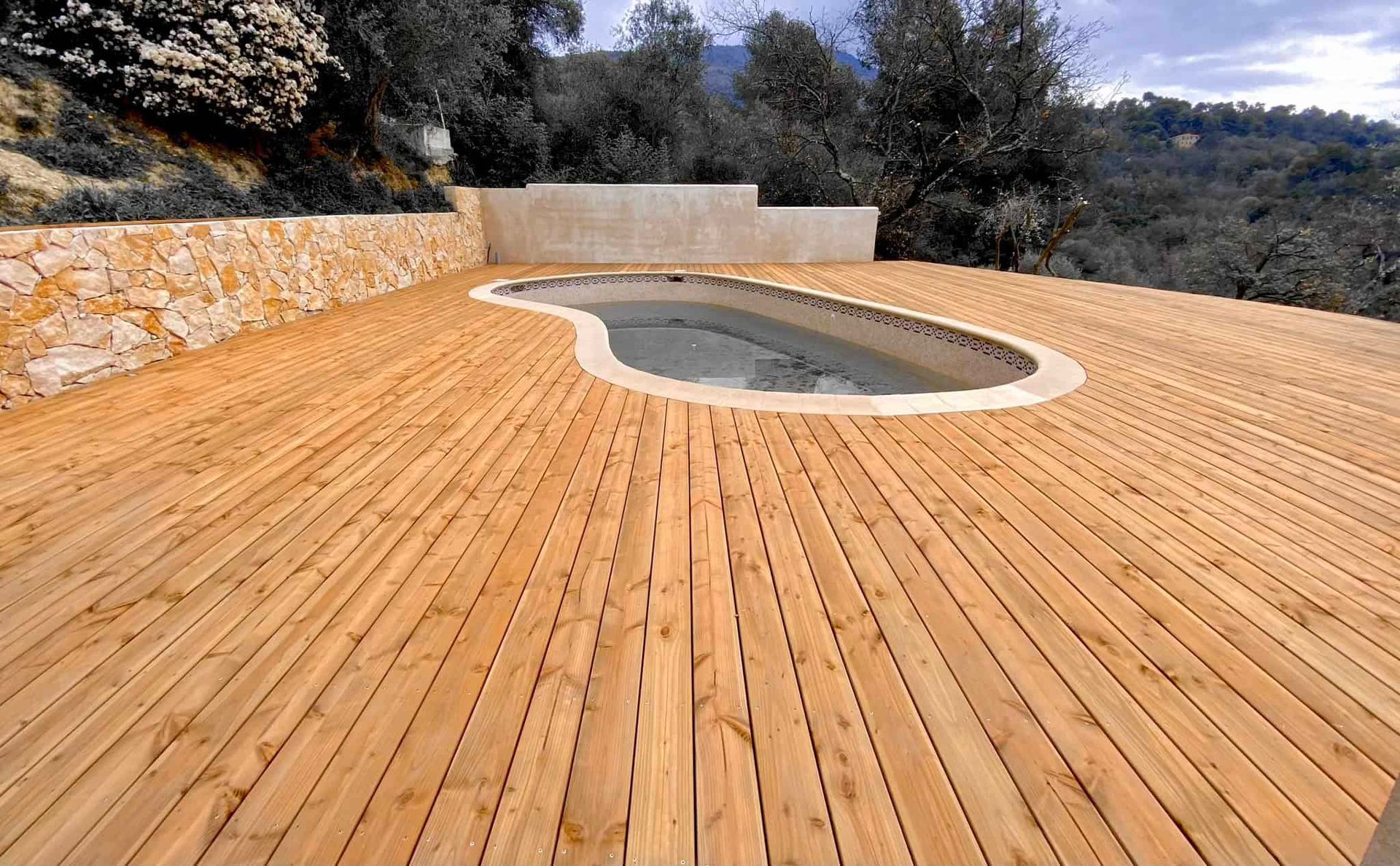 Une terrasse en bois avec une piscine en arrière-plan