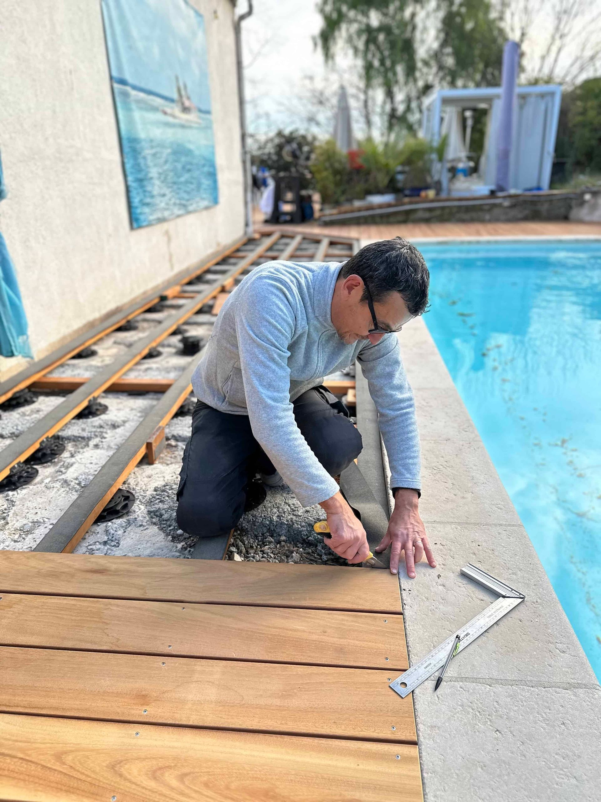 Un homme travaille sur une terrasse en bois à côté d'une piscine.