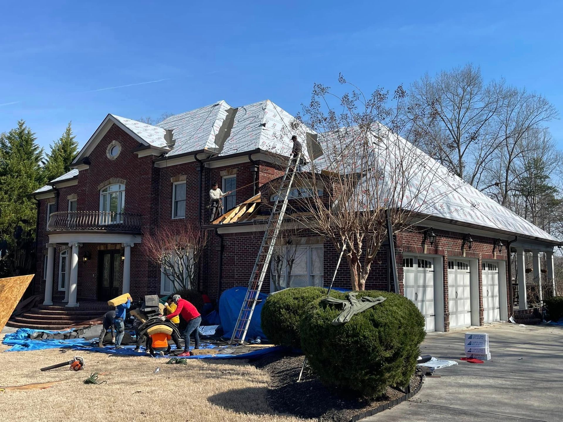 House exterior under renovation with workers, ladders, and materials in the yard