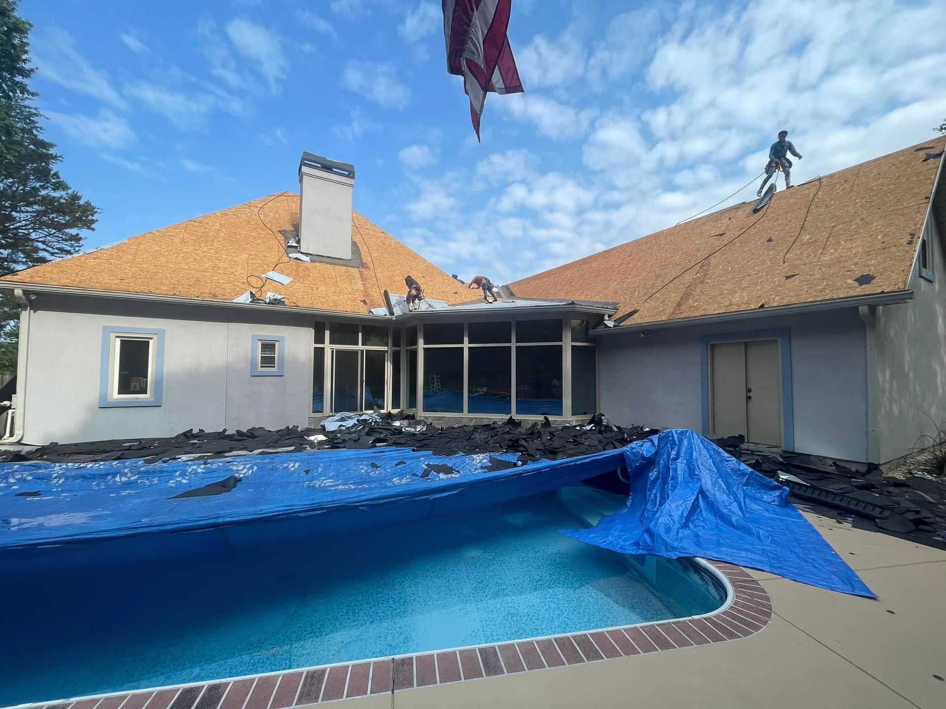 Damaged house with tarp-covered pool area and roof, showing storm cleanup aftermath