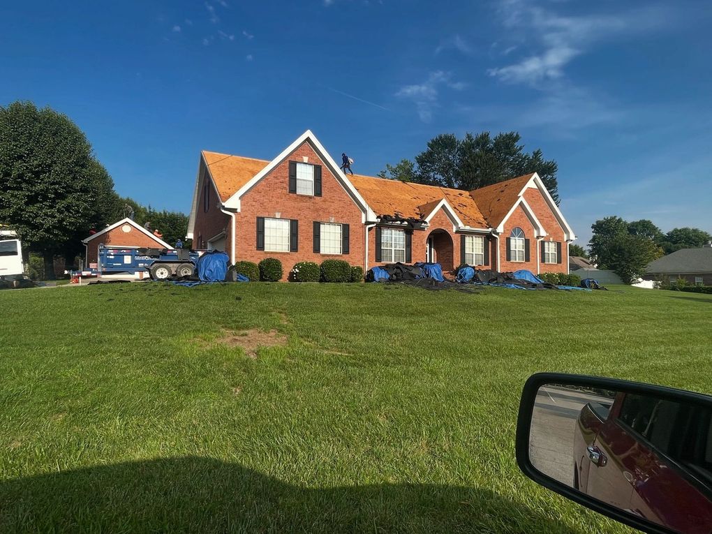 Brick house with white trim on a grassy hill under a blue sky, seen from a car window
