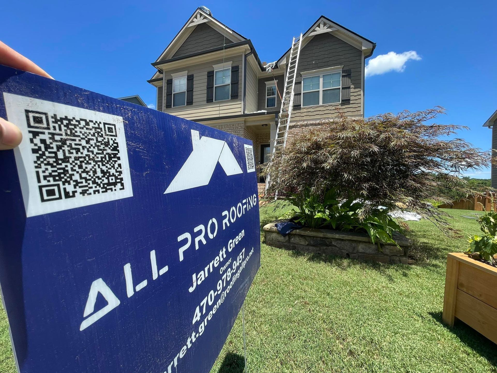 Blue A.L. Pro sign with QR code in front of a stone house under a clear blue sky.
