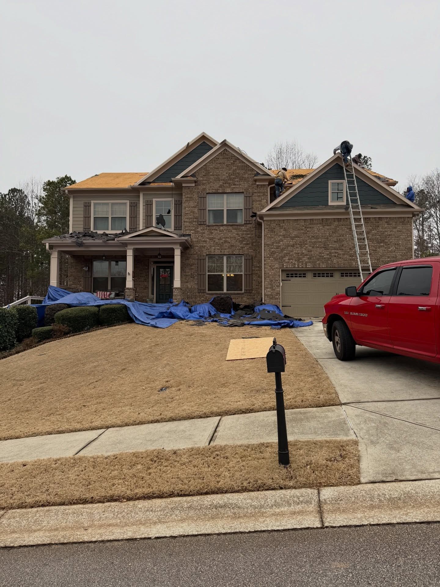 Brick suburban house under construction with blue tarp, gravel yard, and a red pickup truck in front