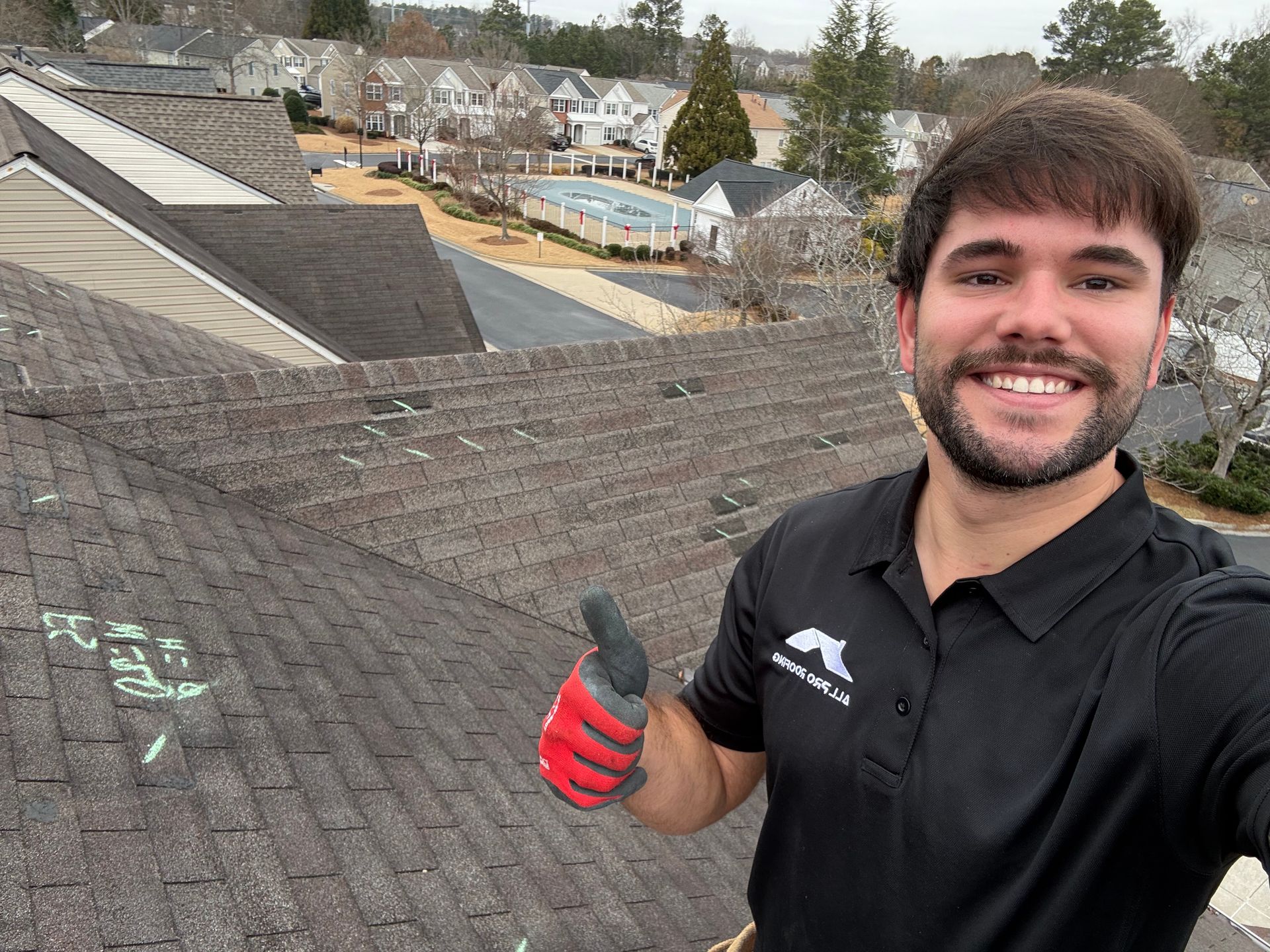 Smiling person in a black shirt and red glove on a rooftop, giving a thumbs-up with houses in the background