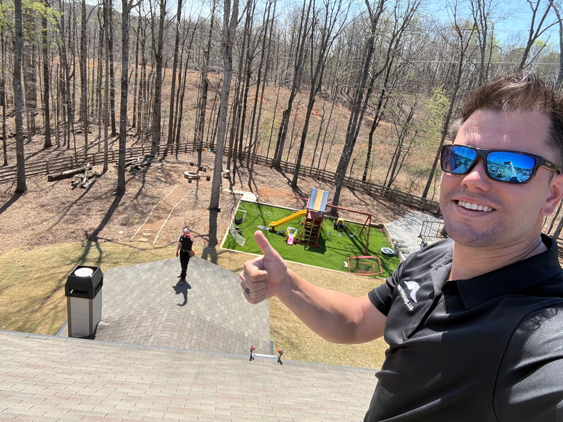 Man in blue sunglasses smiles and points over a backyard deck toward people and a green patio below