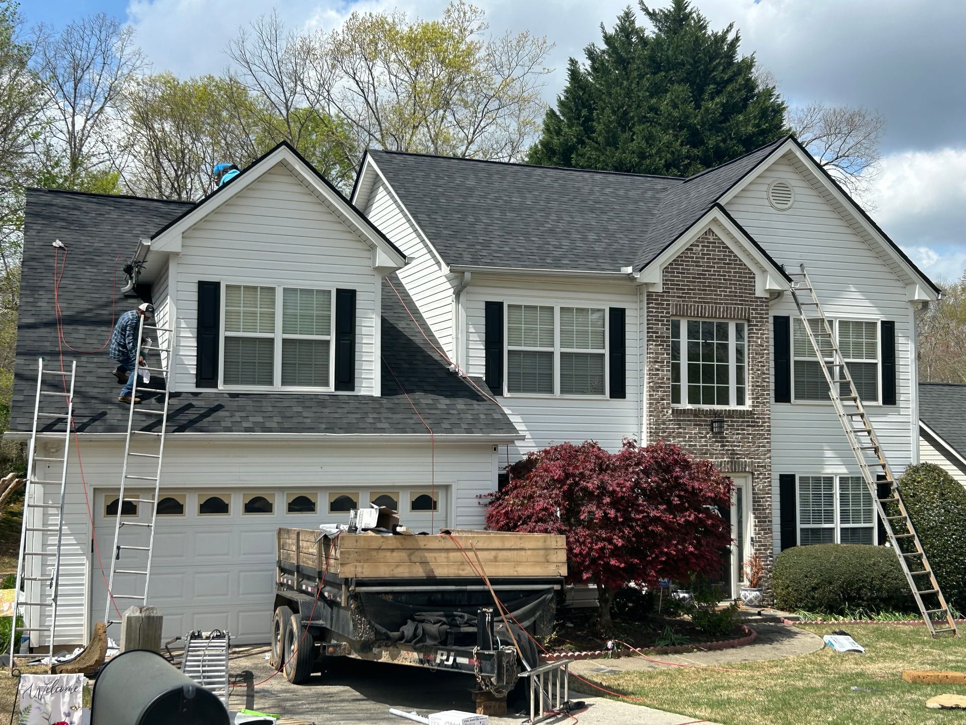 Two-story suburban house with workers on the roof and a dumpster in the driveway