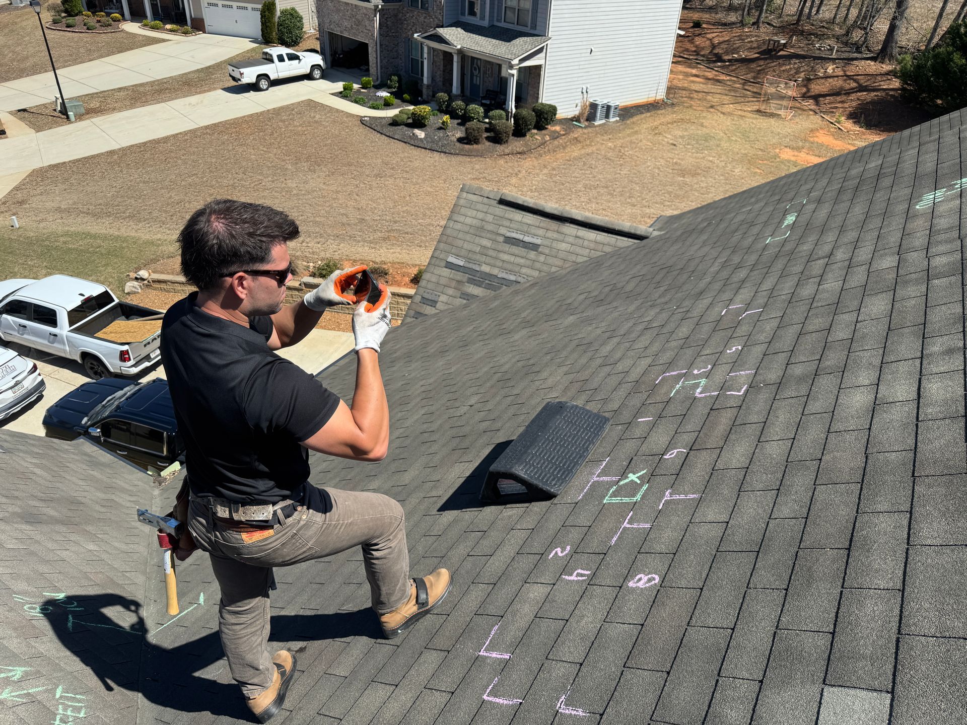 Worker kneeling on a steep roof while applying sealant with a caulk gun