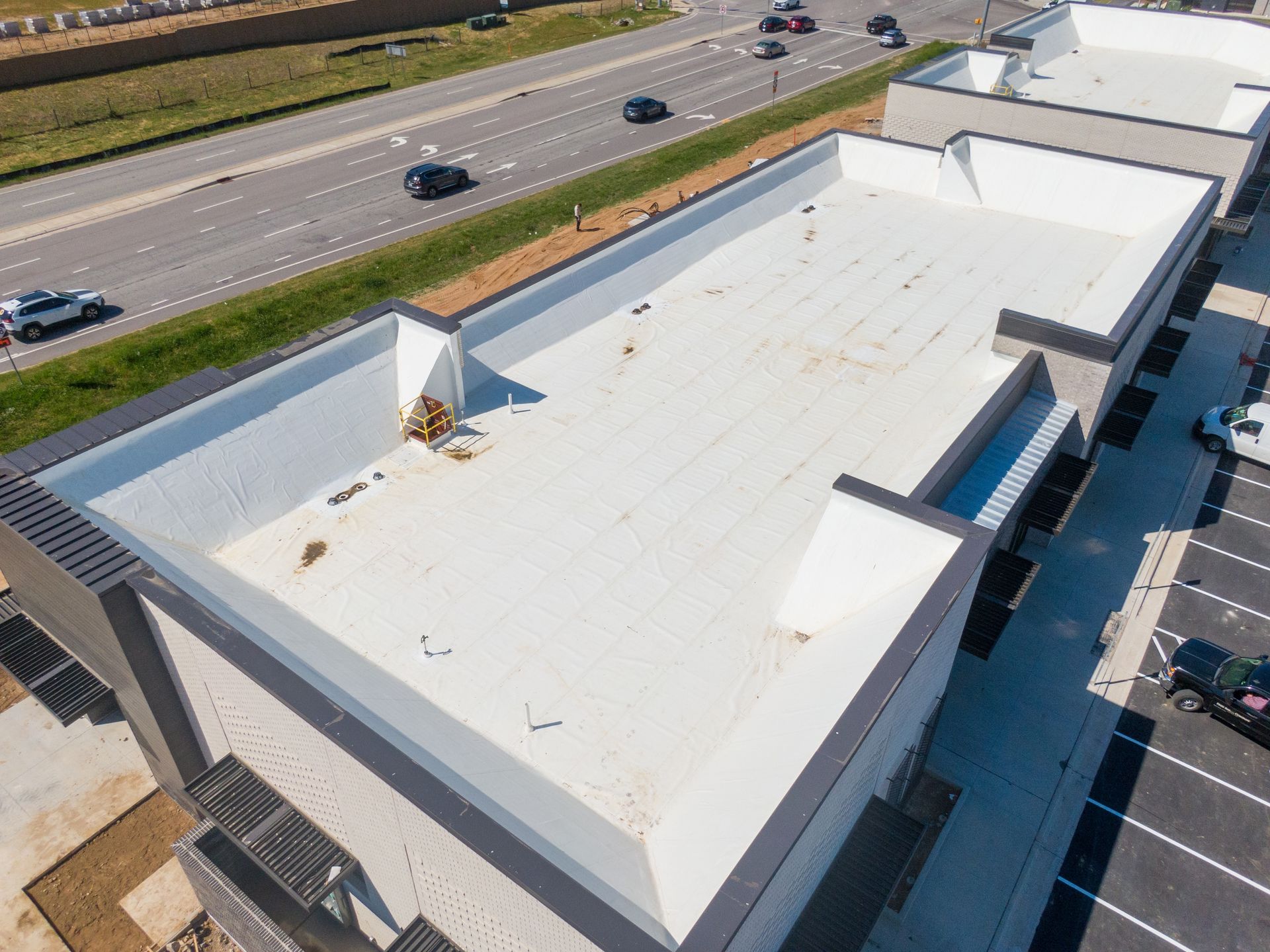 Aerial view of a white flat-roof commercial building beside a highway and parking lot.
