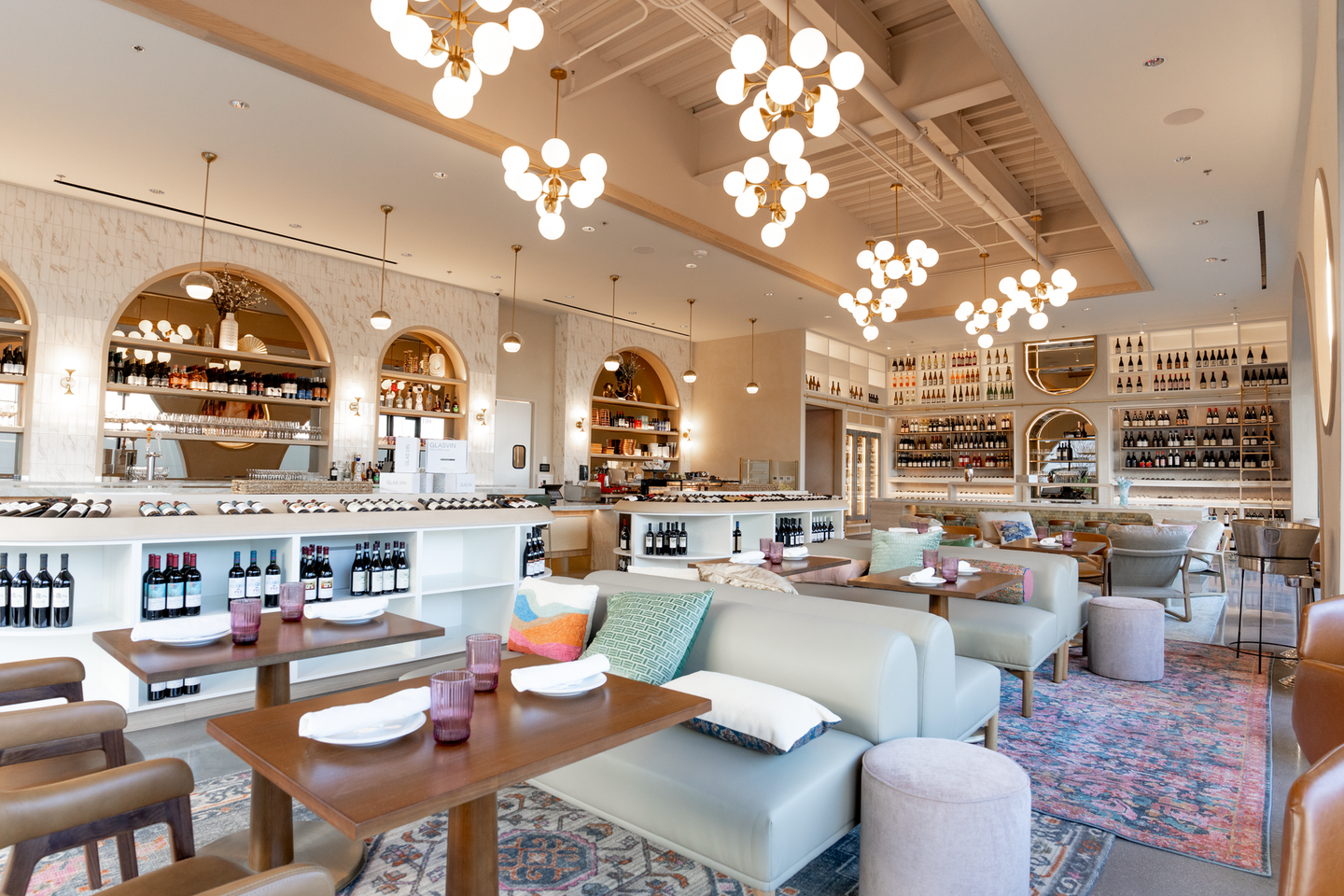 A restaurant with tables , chairs , a couch , and bottles of wine on the shelves.