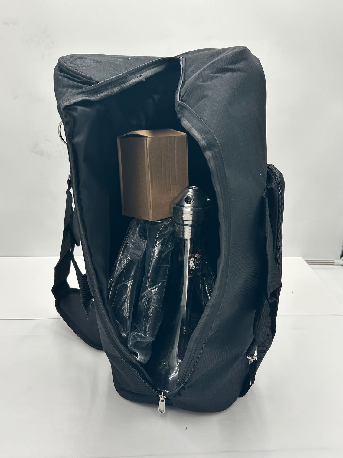 Black backpack with a clear front pocket holding a brown cylindrical item.