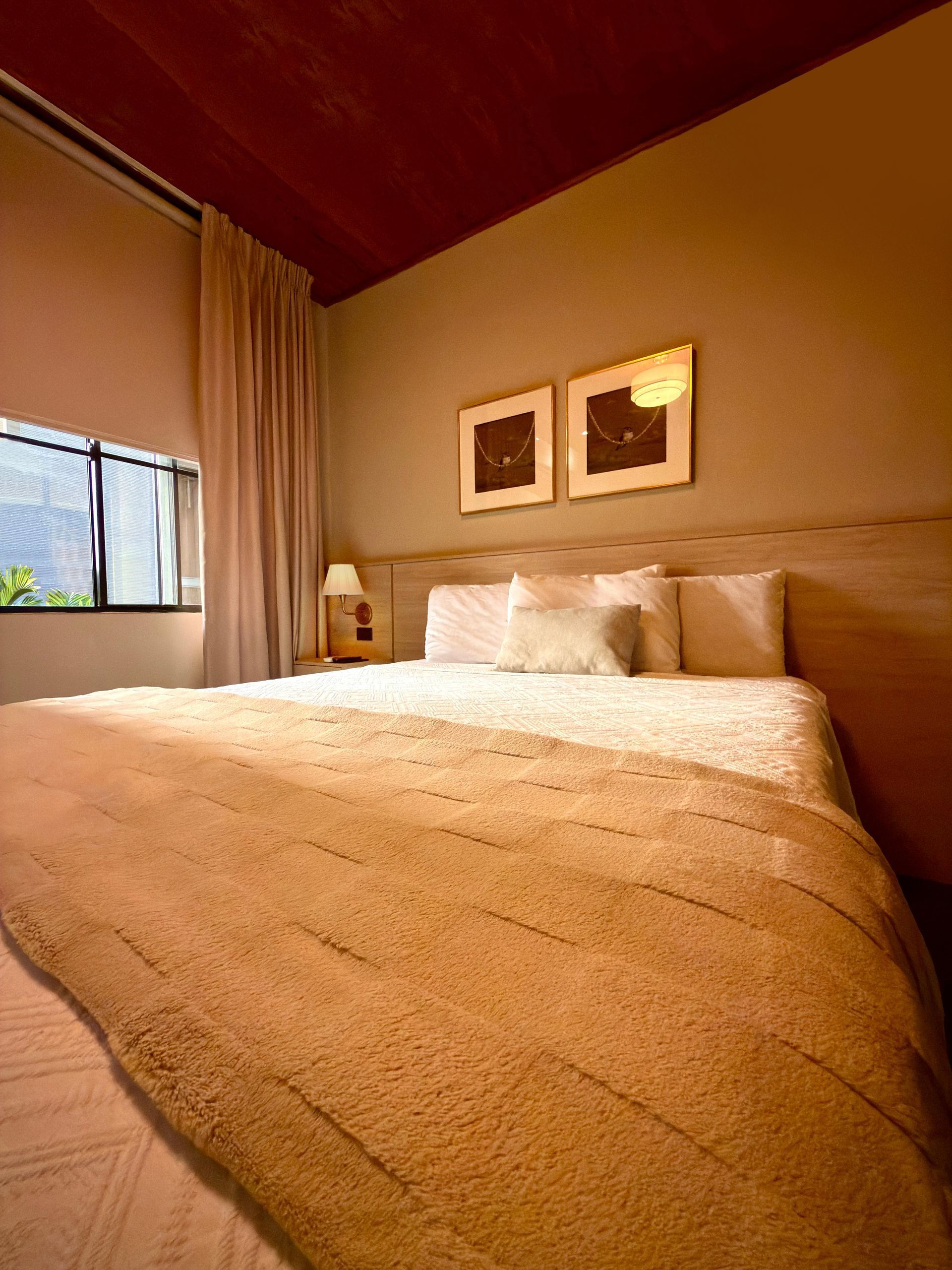 Acogedora habitación con paredes de color beige, cama grande, lámpara de noche y cuadro sobre el cabecero.