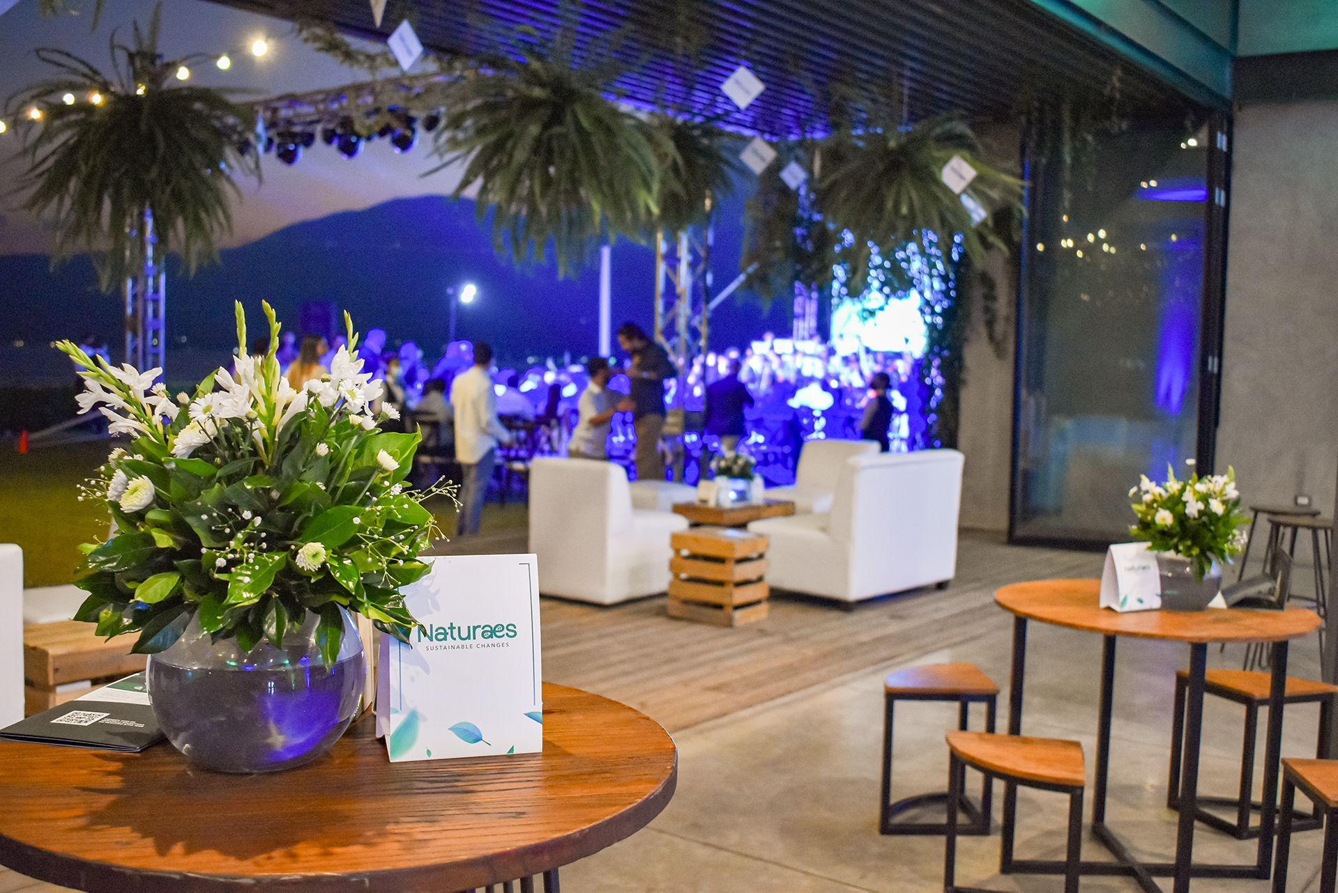 Elegante salón de eventos con sofás blancos, decoración floral e iluminación azul de fondo en el hotel cardedeu coatepeque