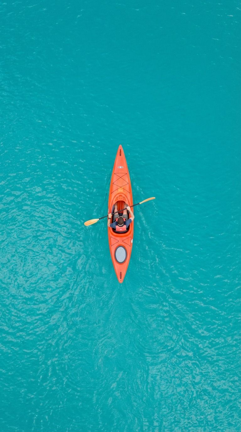 Kayak naranja con un remero en aguas cristalinas de color turquesa, visto desde arriba.