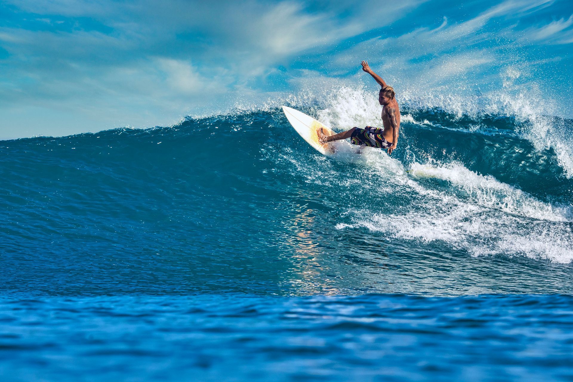 Un surfista cabalga una ola azul, dibujando un giro con espuma en el océano.