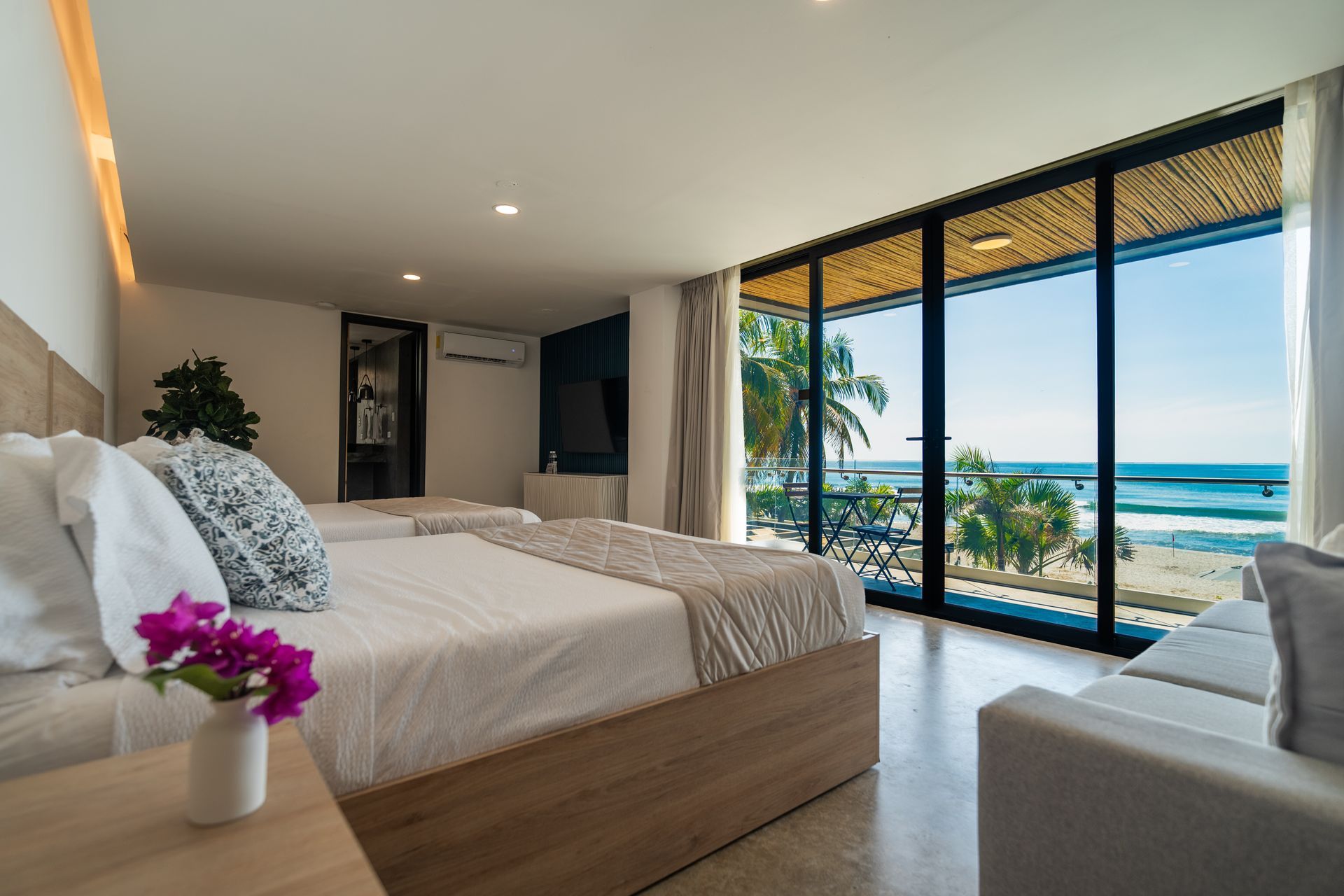 Habitación moderna con cama king size, vistas al océano a través de puertas de cristal y balcón con vistas a las palmeras en cardedeu cangrejera el salvador