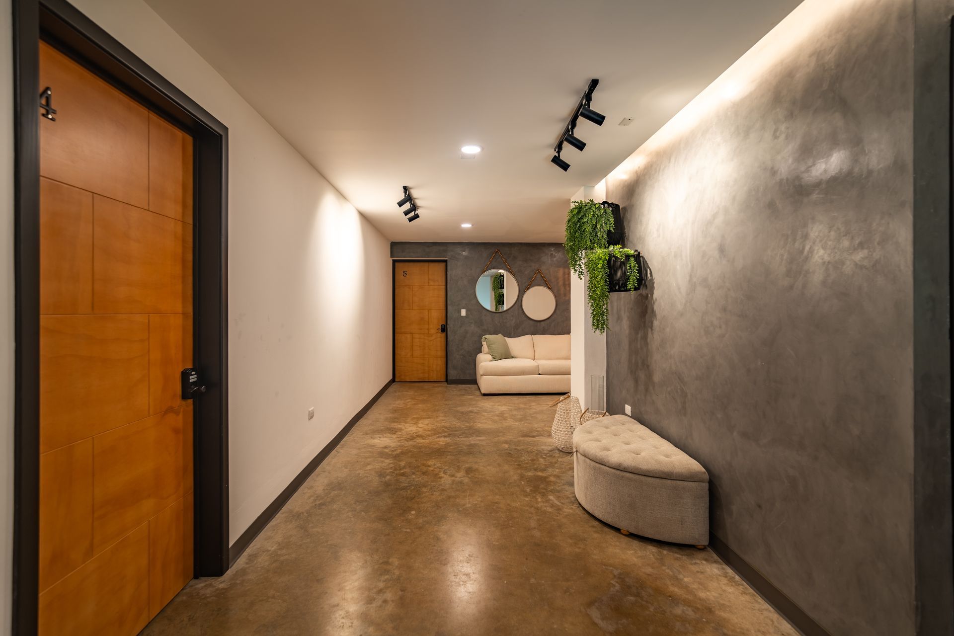 Pasillo moderno con puertas de madera, pared gris, focos en el techo y un banco con una planta al final en cardedeu cangrejera el salvador