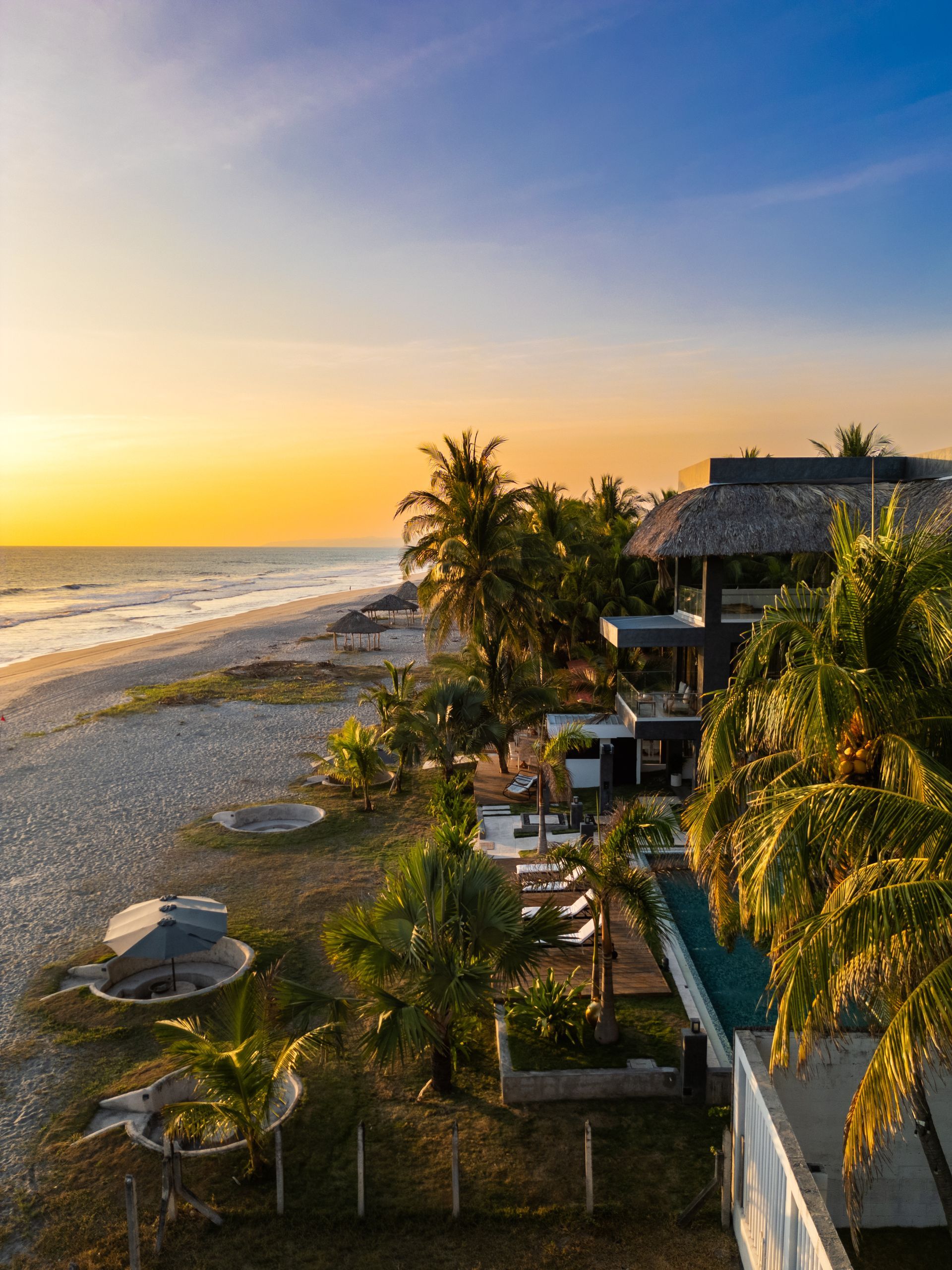Cardedeu cangrejera el salvador frente al mar al atardecer, con palmeras, olas del océano y una piscina junto a la playa de arena.