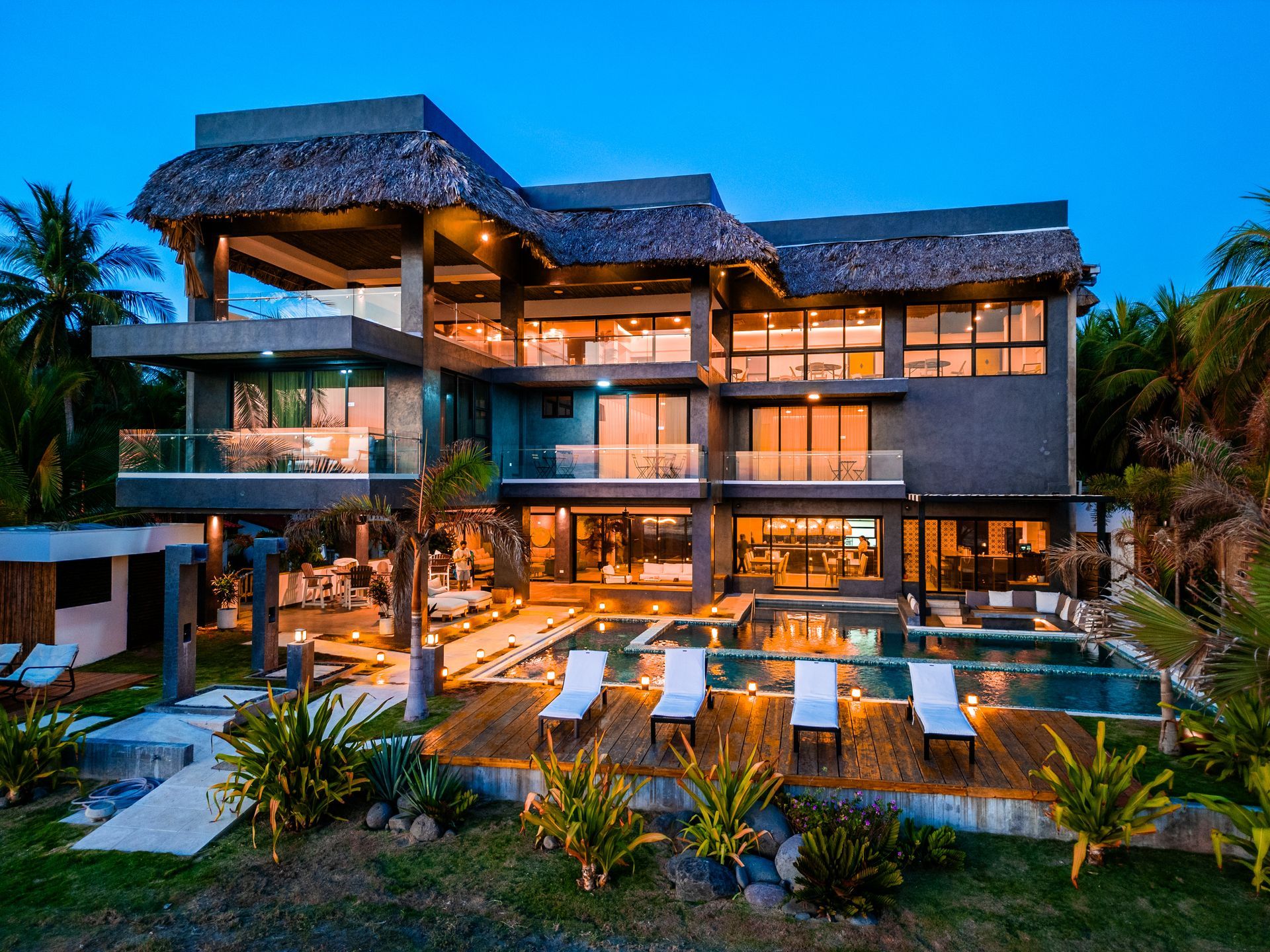 Residence Cardedeu cangrejera el salvador frente al mar al atardecer con luces brillantes, palmeras y una terraza junto a la piscina con vistas al océano.