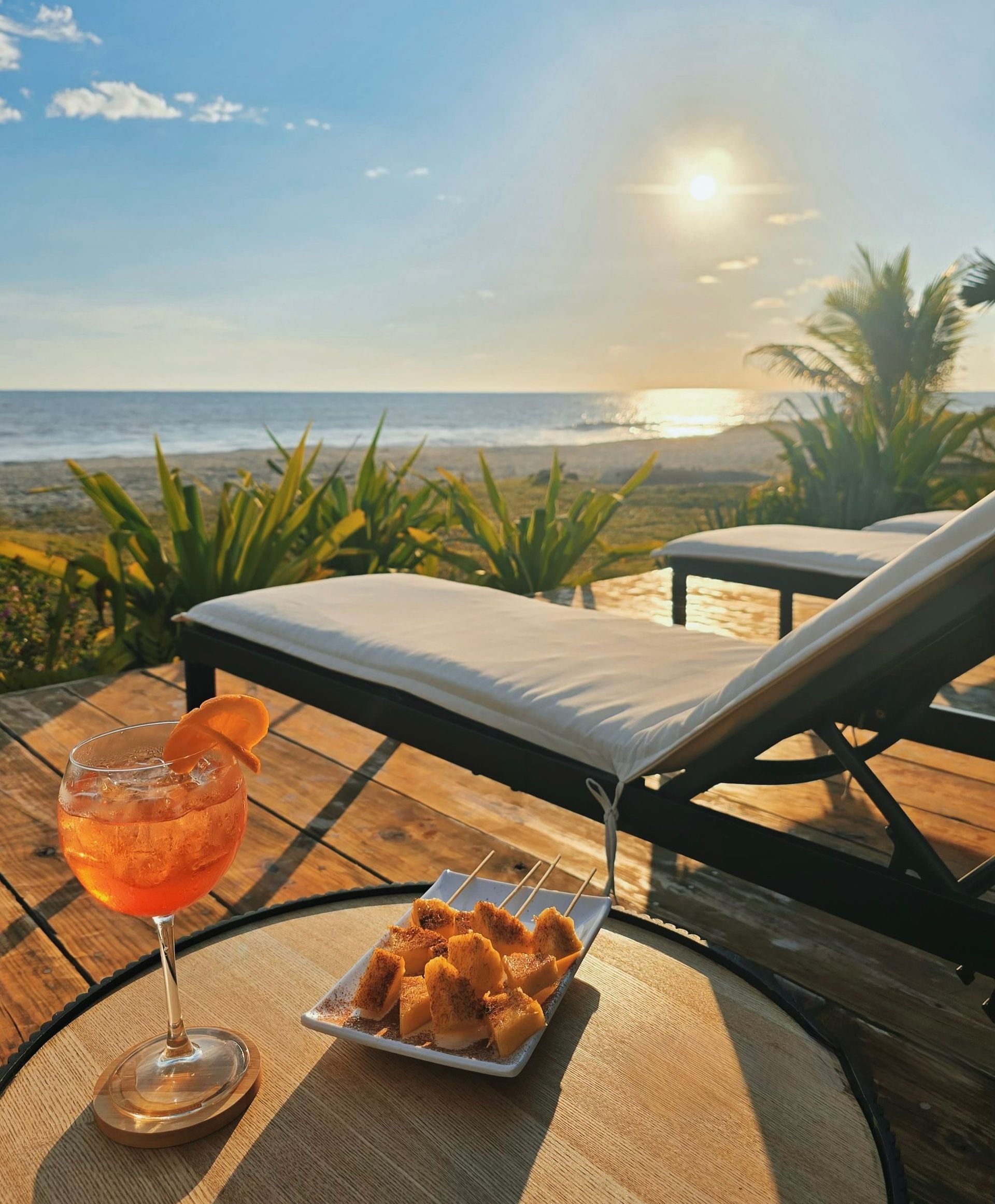 Tumbona frente a la playa al atardecer con una bebida tropical y pasteles sobre una mesa, vista al océano en cardedeu cangrejera el salvador