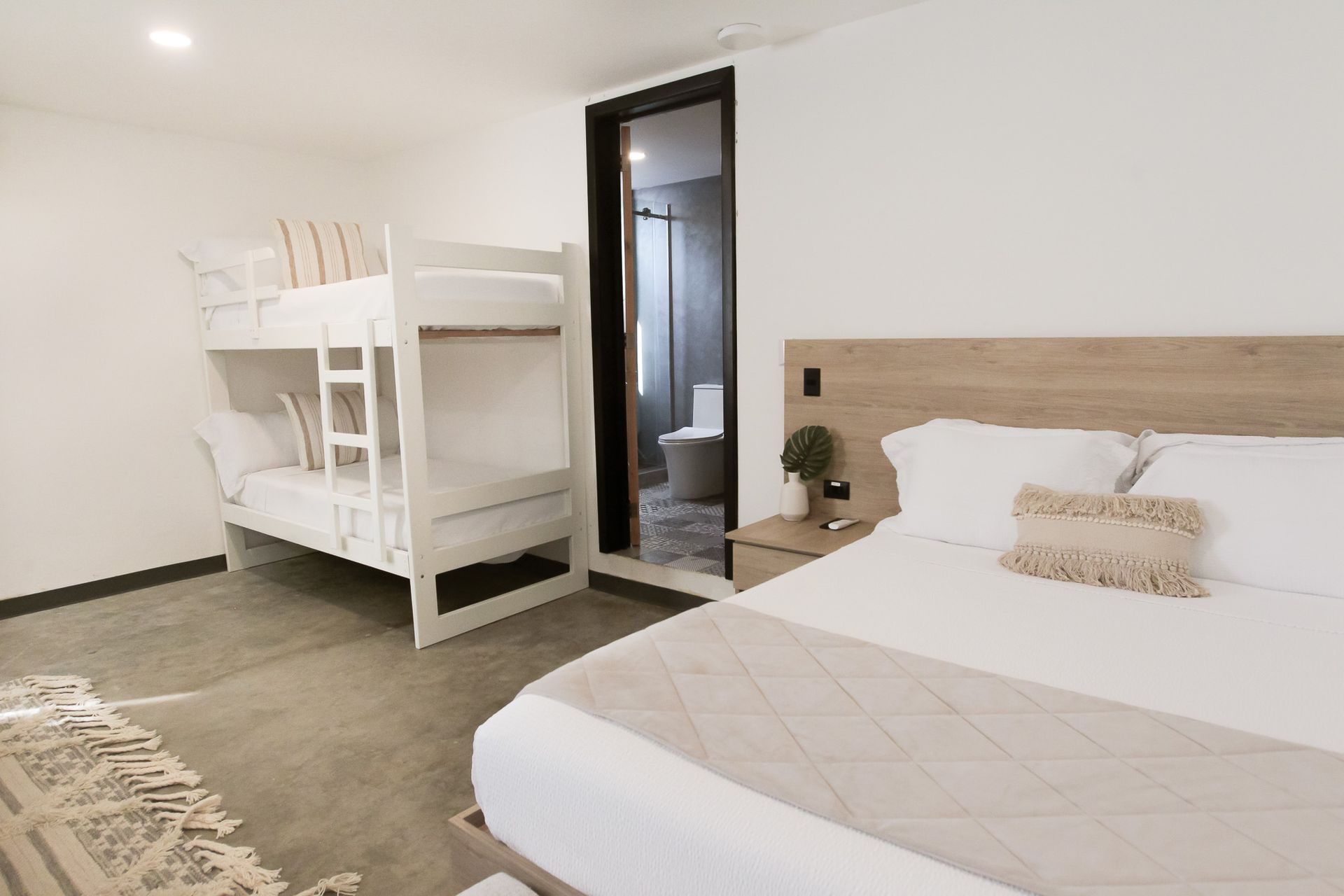 Habitación luminosa con litera, cama de matrimonio y puerta de baño abierta.