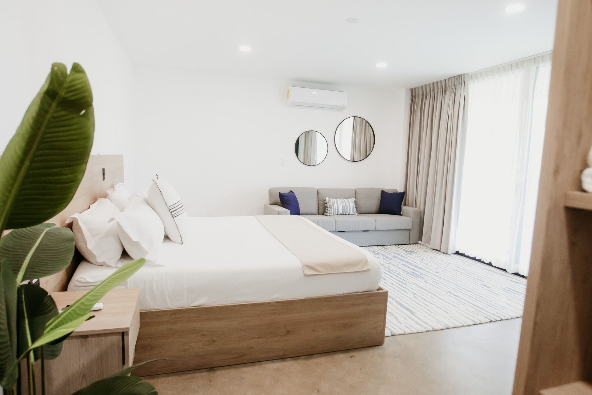 Habitación luminosa y moderna con cama blanca, sofá gris, espejos redondos en la pared y cortinas que van del suelo al techo en cardedeu cangrejera el salvador