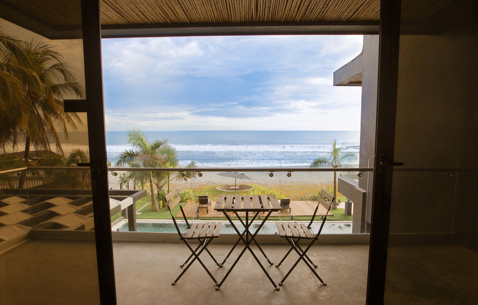 Vista desde el balcón del océano y la playa con una pequeña mesa y sillas en primer plano.