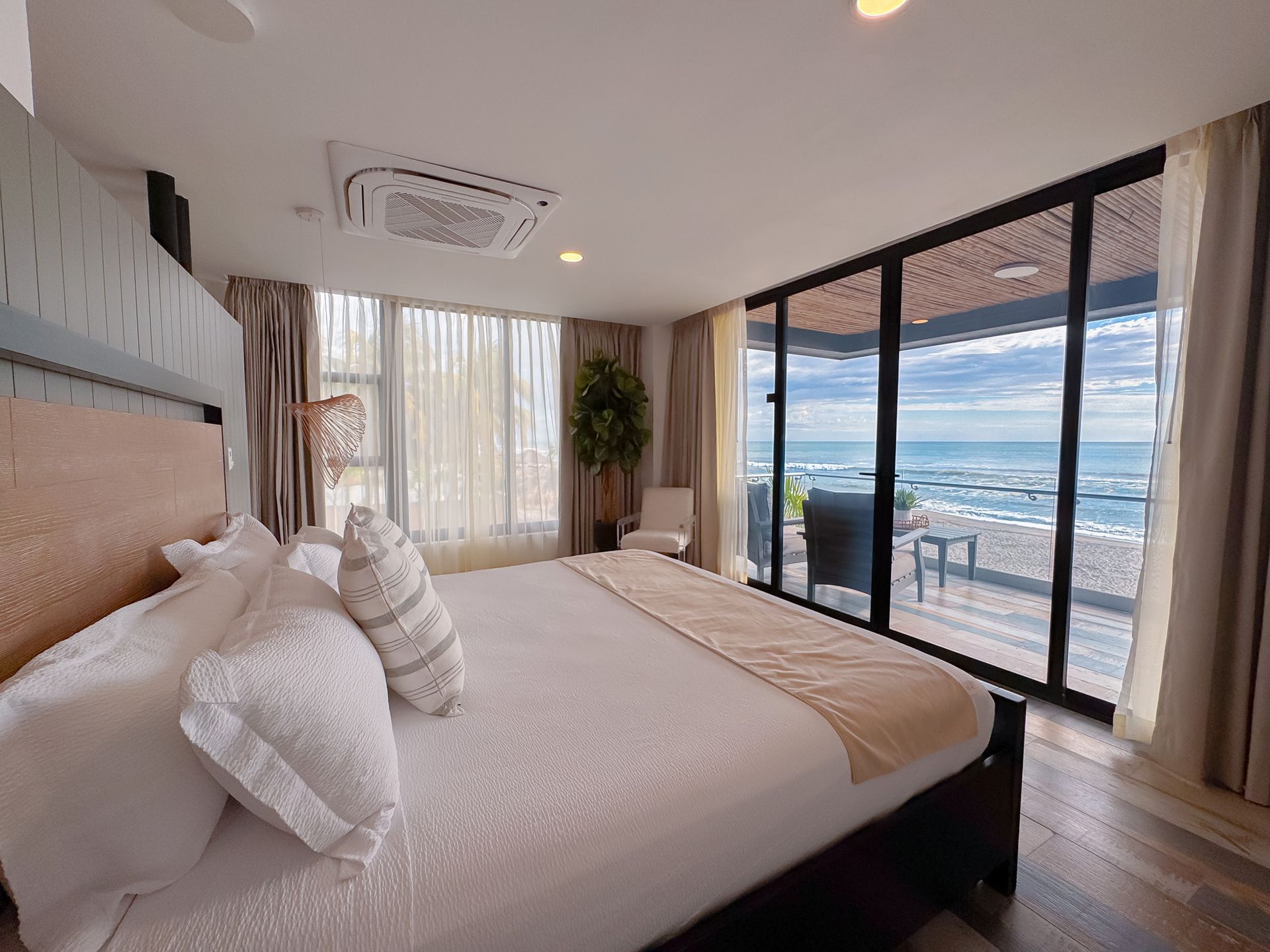 Dormitorio moderno con vistas al mar, cama grande y puertas correderas de cristal del suelo al techo.