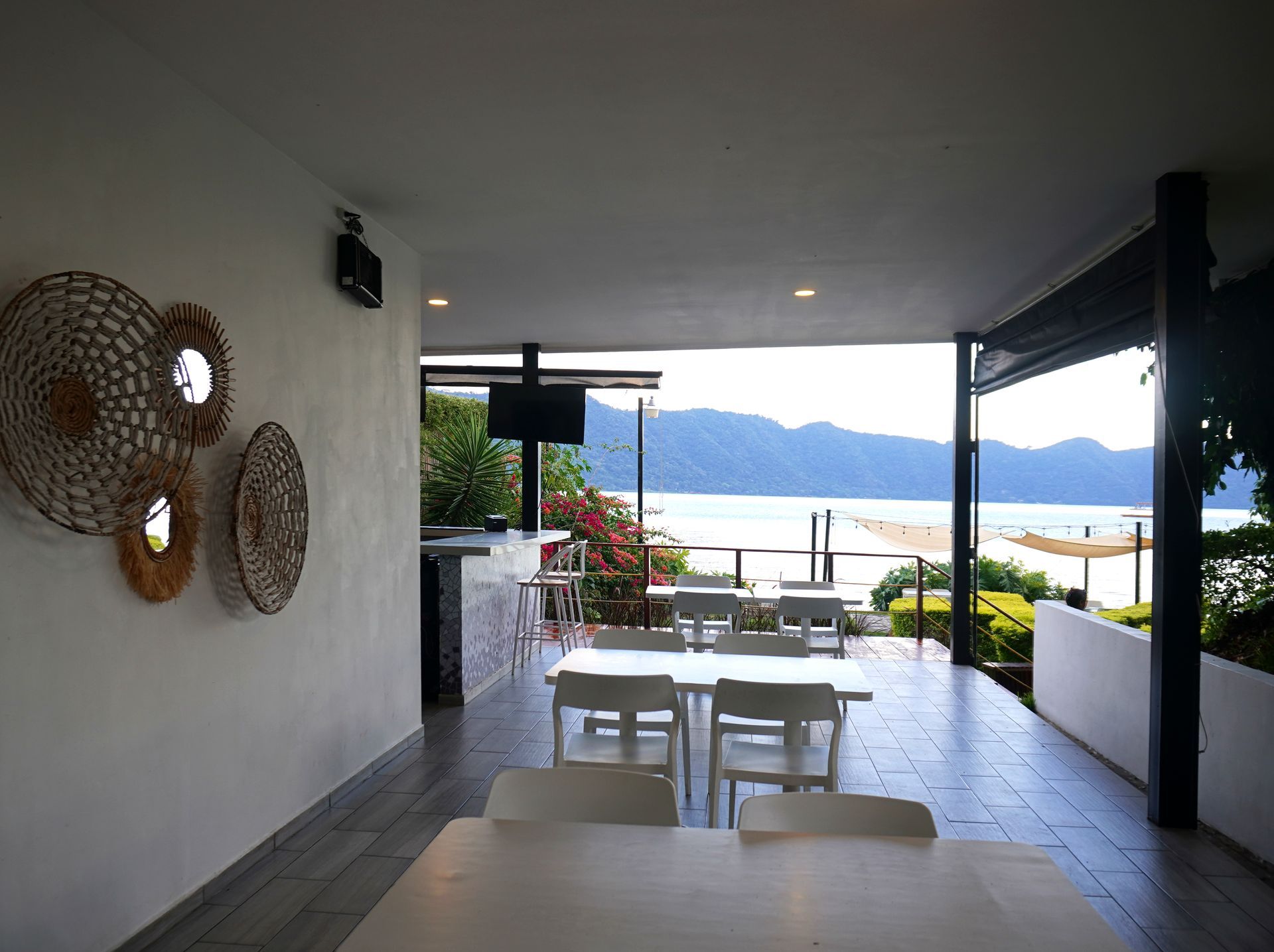Patio cubierto con mesa y sillas blancas, decoración de pared tejida y vistas al océano y a las montañas  en restaurante bistro hotel coatepeque