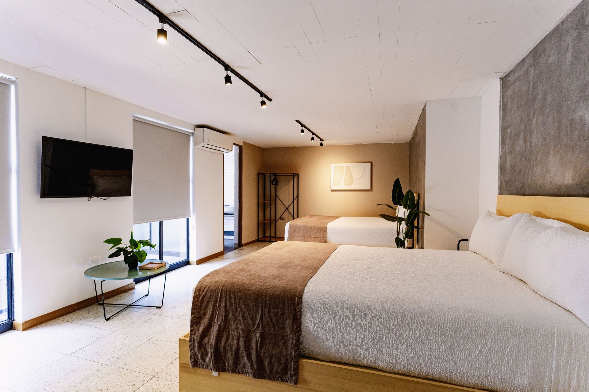 Habitación luminosa y moderna con una cama grande, televisor montado en la pared, ventanas y una decoración cálida y neutra en hotel cardedeu express