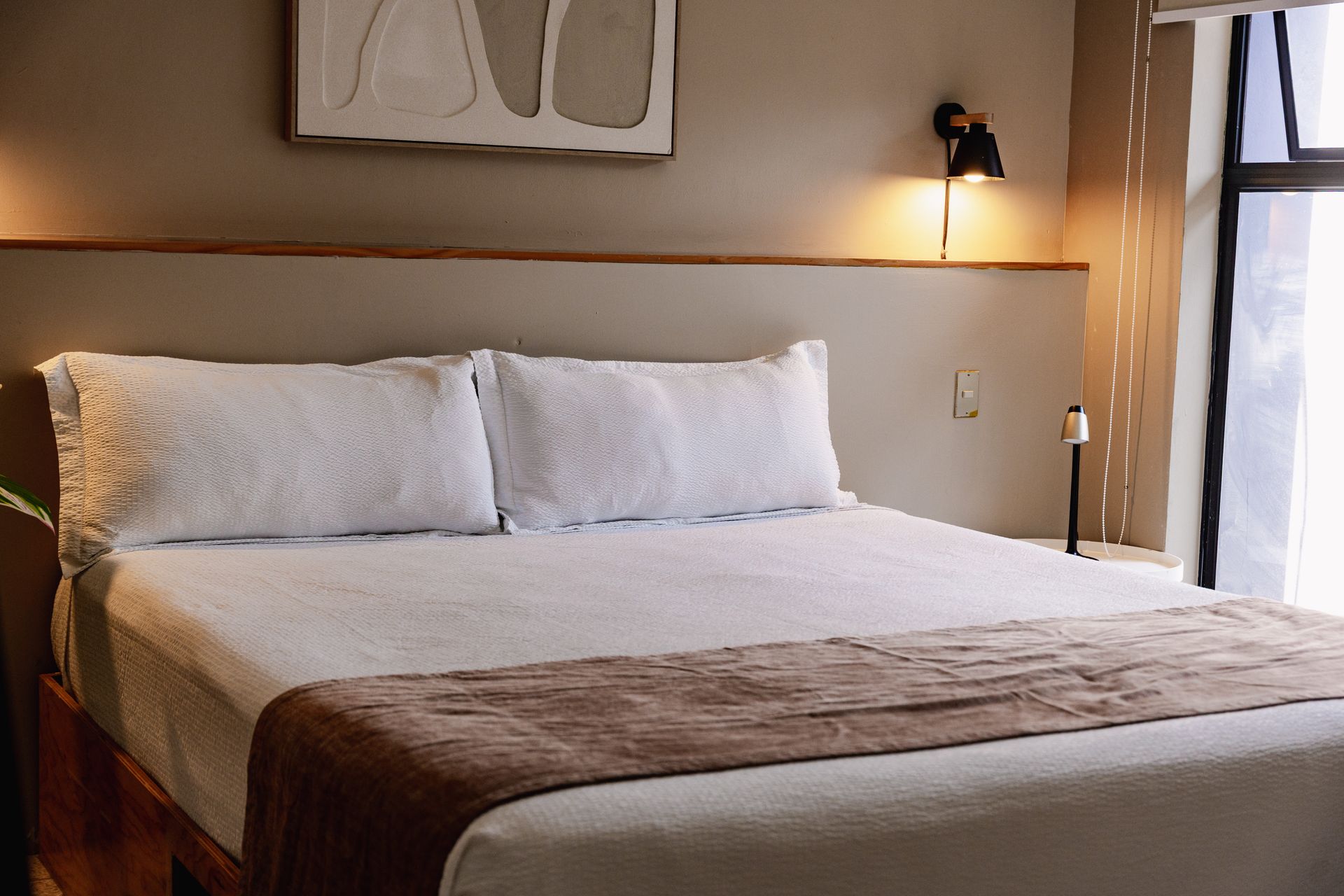 Cama bien hecha con sábanas blancas y una manta marrón en un dormitorio acogedor con iluminación cálida en hotel cardedeu express