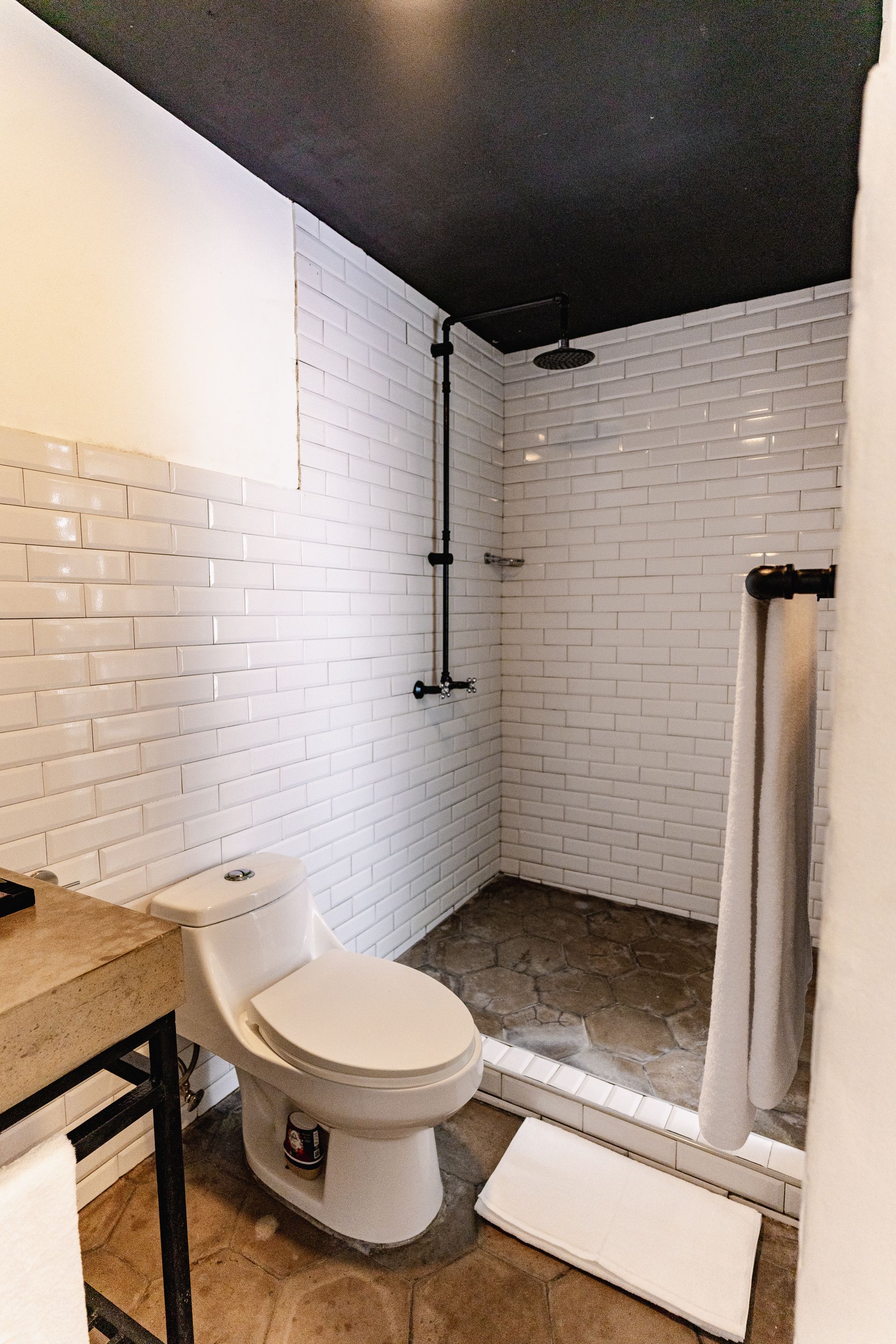 Baño pequeño con paredes revestidas de azulejos blancos tipo metro, techo negro, inodoro, ducha y toallas dobladas en hotel cardedeu express