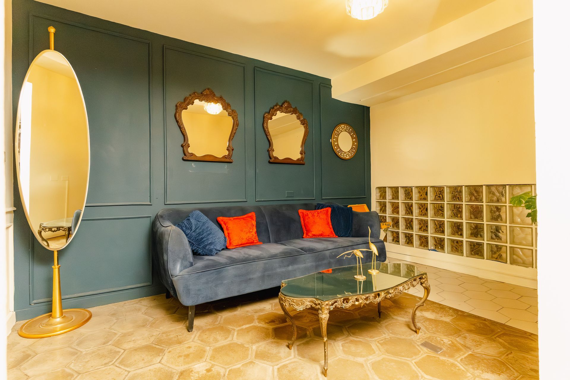 Elegante sala de estar con pared revestida de paneles color verde azulado, sofá de terciopelo azul, espejo dorado y mesa de centro de mármol.