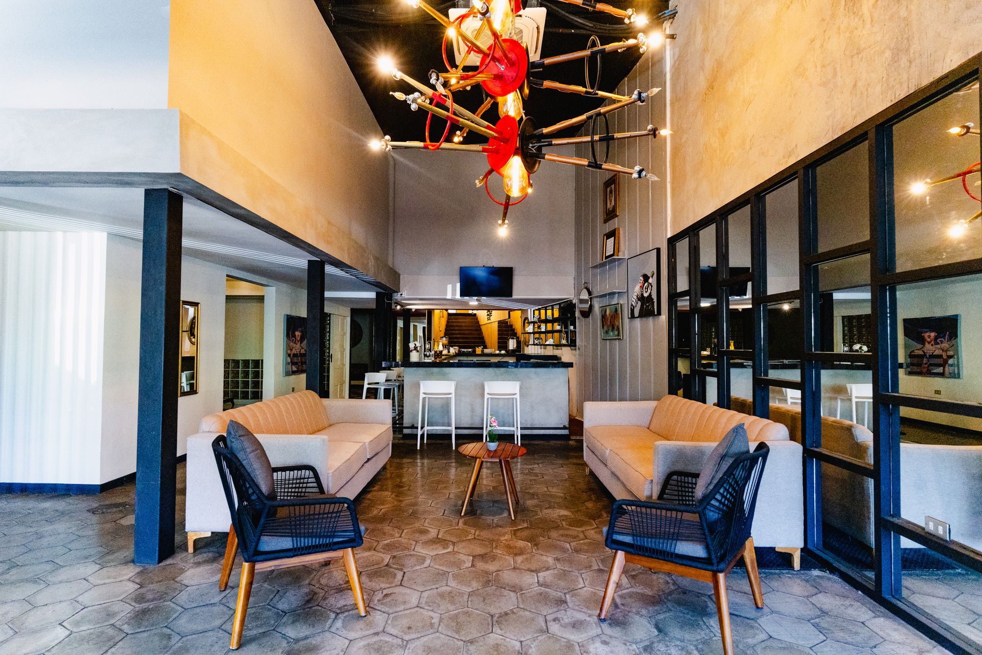 Vestíbulo moderno con paredes de vidrio con marcos negros, asientos color canela, piso de baldosas estampadas y decoración de techo roja.