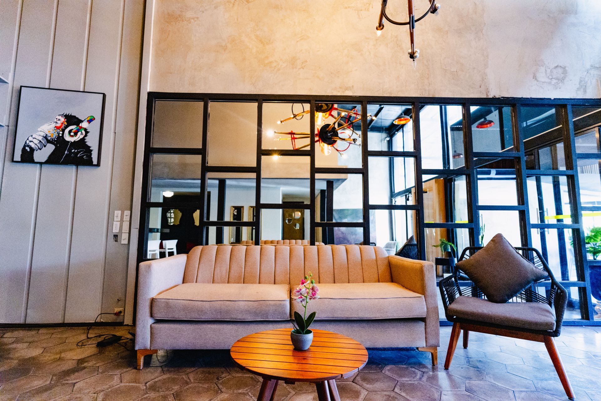 Salón moderno con sofá beige, mesa de centro naranja y zona de estar con mampara de cristal con marco negro.