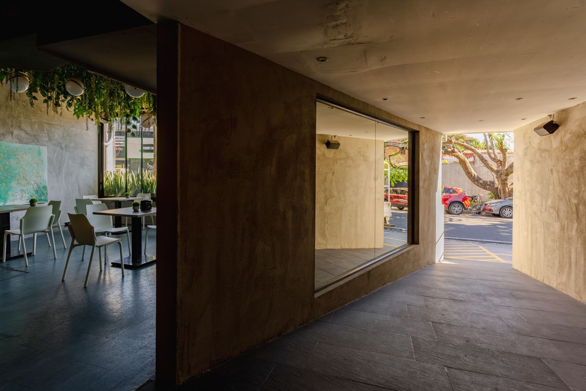 Pasarela exterior cubierta junto a una cafetería, con mesas a la izquierda y coches aparcados visibles al frente.
