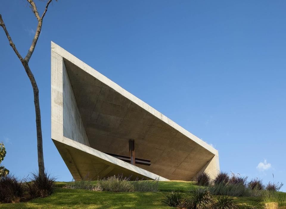Capilla blanca moderna con techo inclinado en una colina cubierta de hierba bajo un cielo azul en hotel cardedeu coatepeque