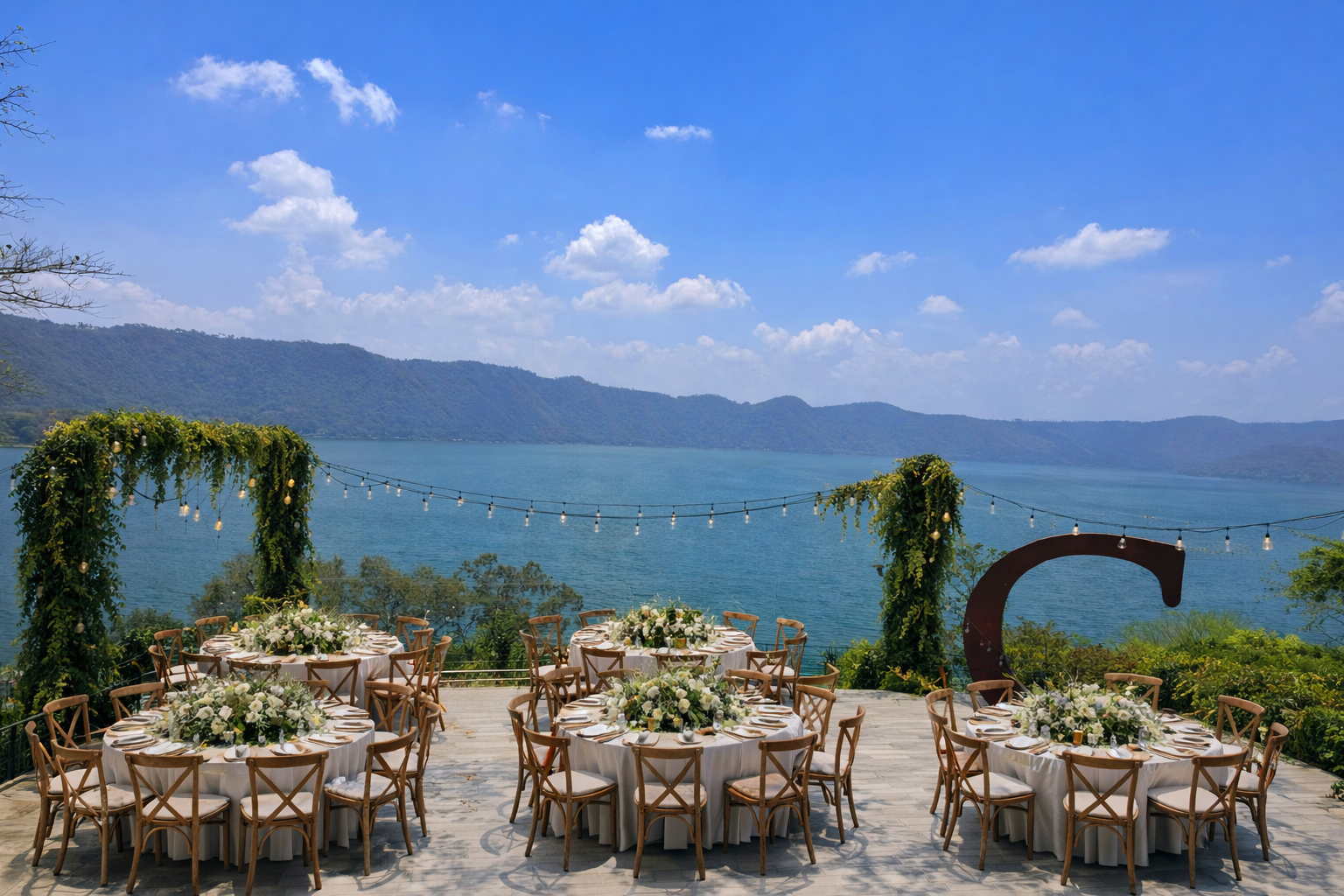 Comedor al aire libre junto al mar con mesas y sillas de madera con vistas a una bahía azul y a las montañas en el hotel cardedeu coatepeque