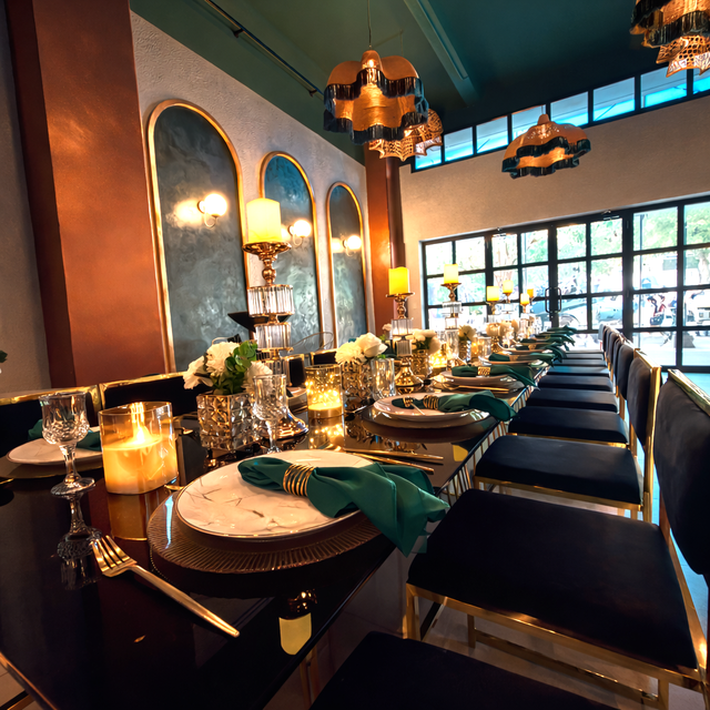 Elegante mesa de comedor de restaurante silvestre con velas, sillas oscuras, servilletas color turquesa y cálida iluminación colgante.
