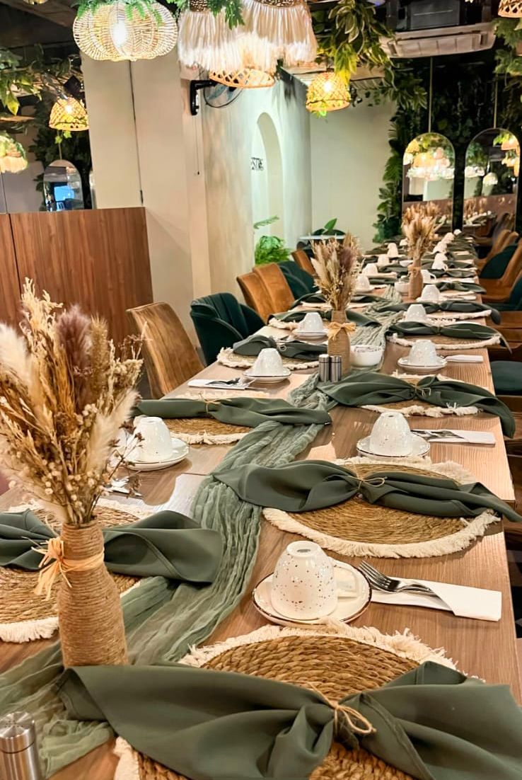 Mesa de comedor larga con servilletas verdes, manteles individuales tejidos, velas y decoración floral seca bajo luces colgantes en restaurante silvestre san benito