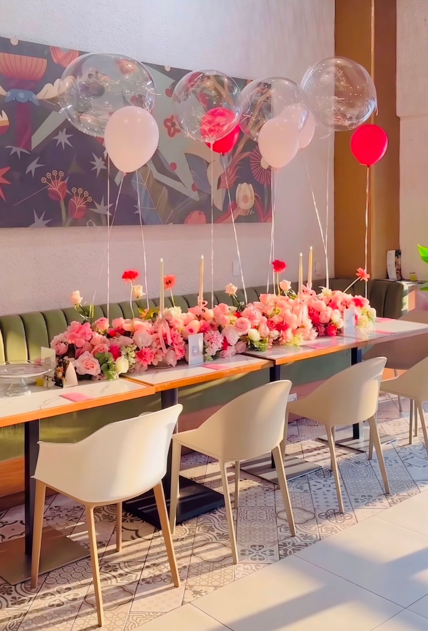 Mesa de banquete decorada con flores rosas, velas y globos rojos y blancos en una habitación luminosa.