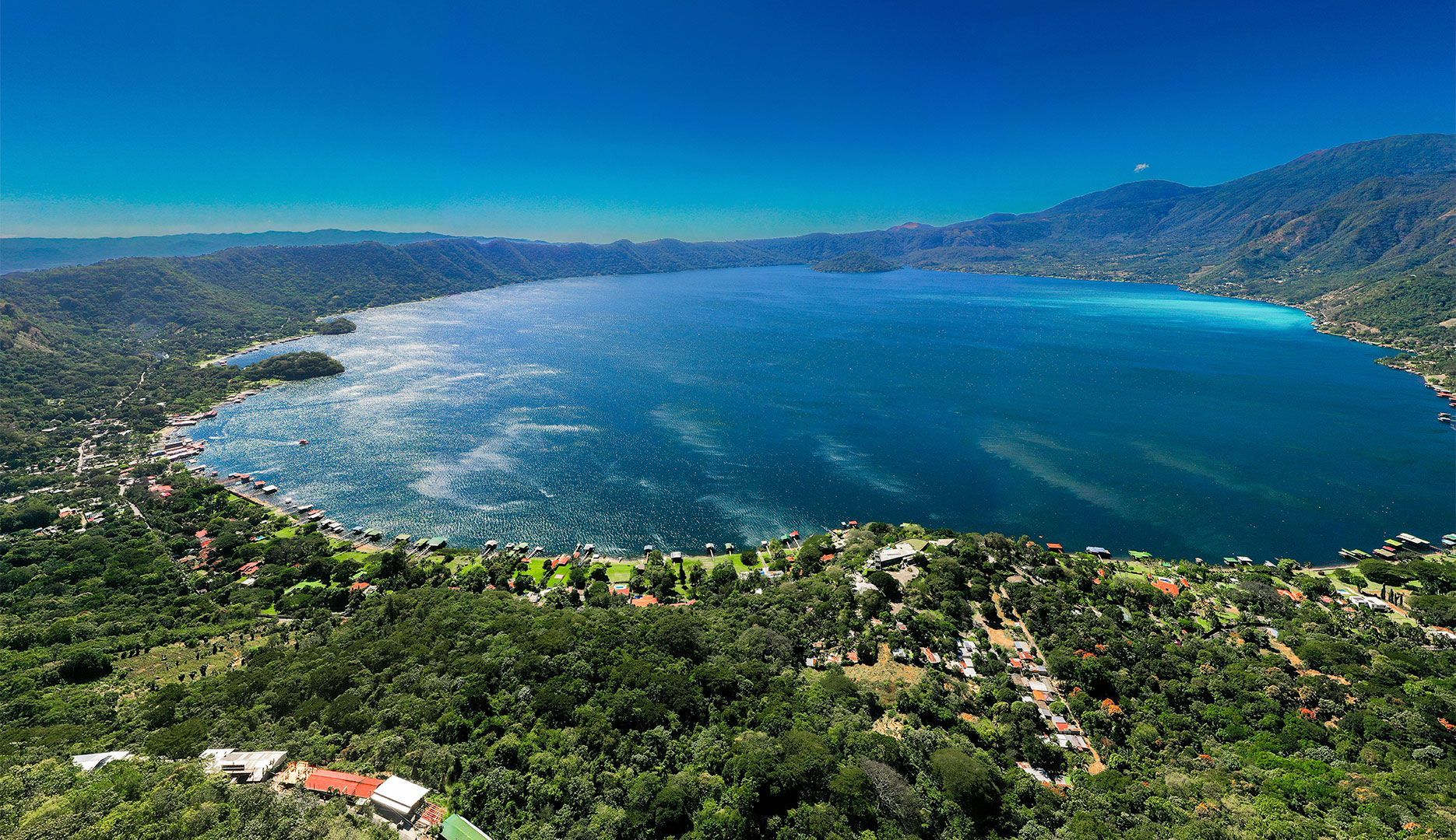 Vista aérea de una amplia bahía azul bordeada de verdes colinas y un pueblo costero en el lago coatepeque el salvador