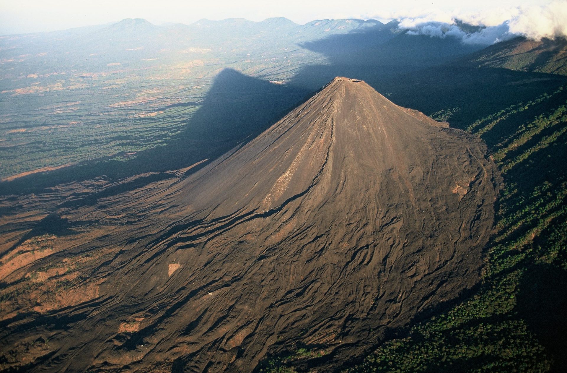 Vista aérea de un escarpado cono volcánico que se eleva desde un valle verde bajo montañas brumosas en volcan de izalco el salvador