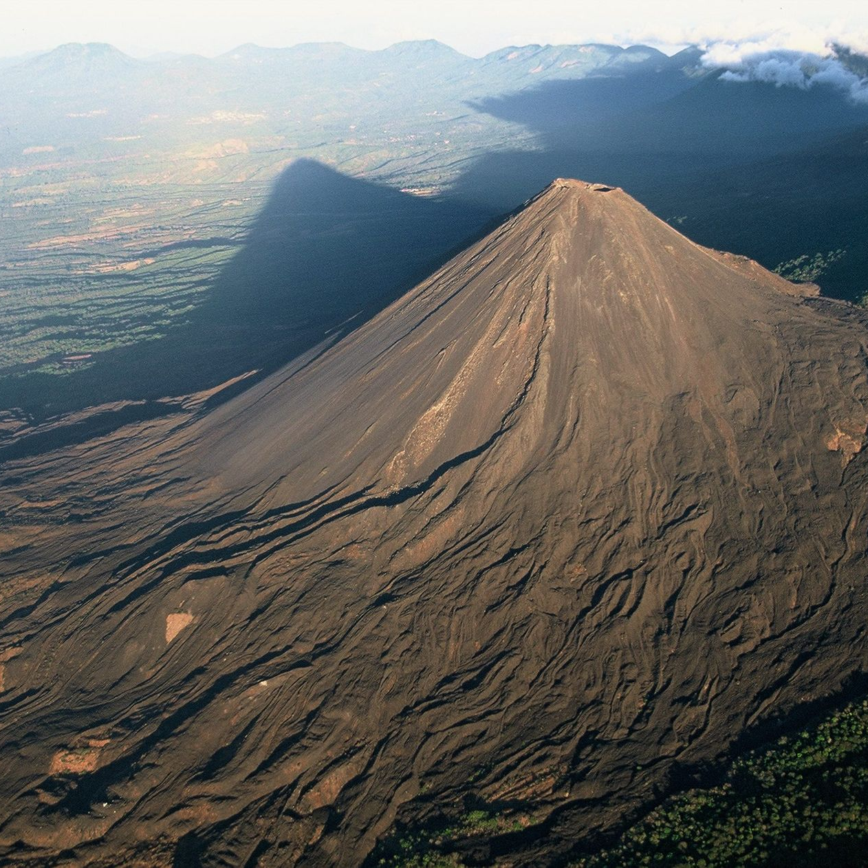 Un escarpado cono volcánico con laderas de ceniza que se elevan sobre un valle verde y montañas distantes en el volcan de izalco en el salvador