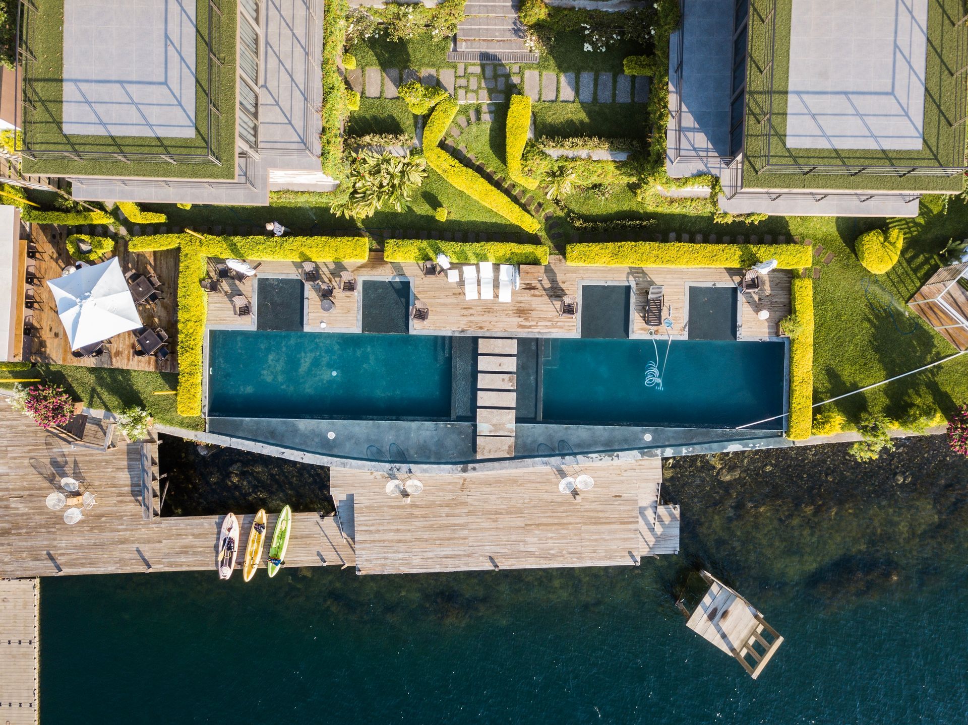 Vista aérea residence cardedeu coatepeque con dos piscinas azules junto a un muelle de madera y agua cristalina debajo.